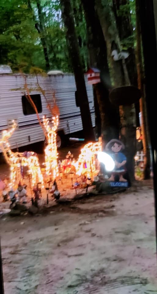 Outdoor decorative lights glowing beside a trailer in a wooded area at dusk
