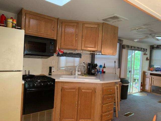 Small kitchen with wooden cabinets, white refrigerator, black stove, and a window looking out to greenery.
