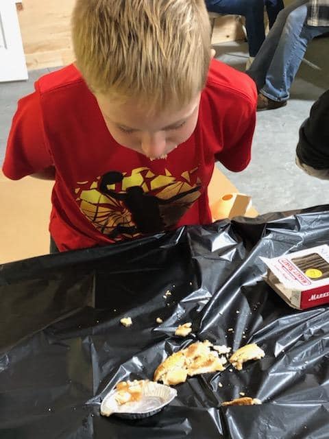 Child in a red shirt leans over a table with a black tablecloth and spilled food or dessert.