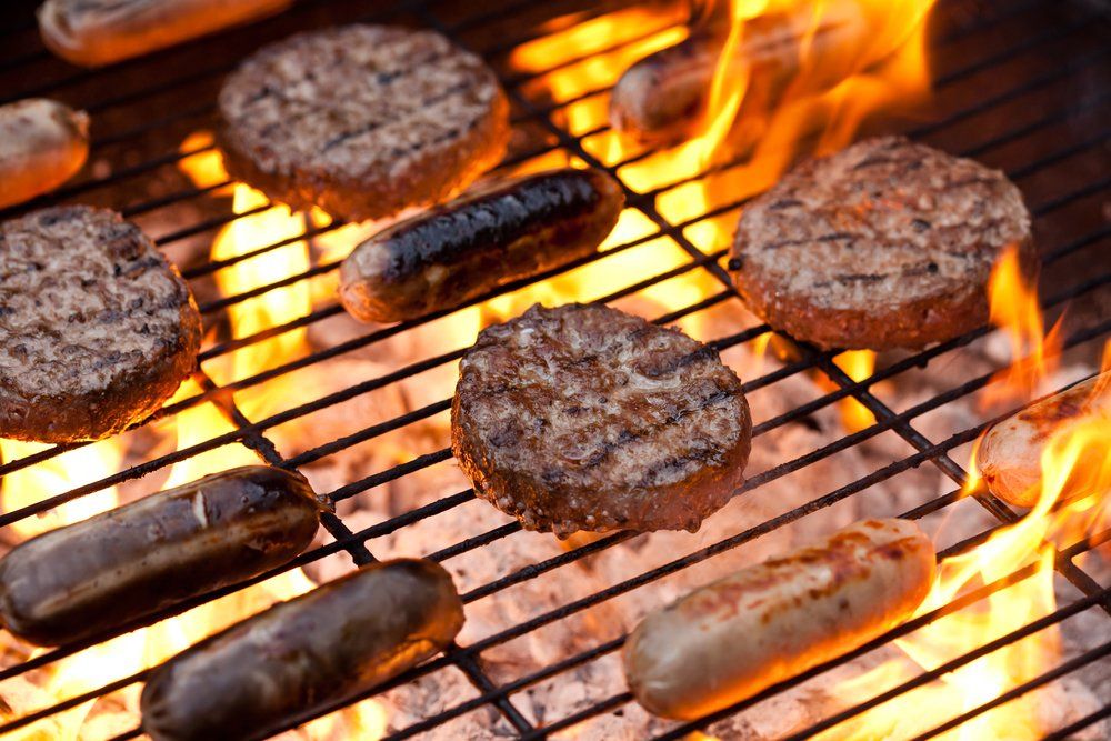 Burger patties and hot dogs grilling over open flames on a barbecue grill
