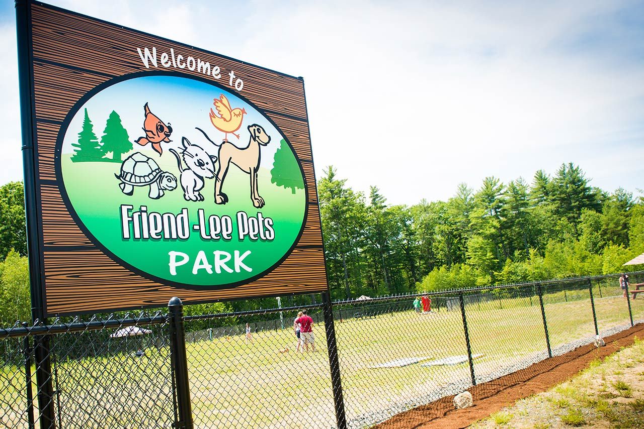 Entrance sign for Friendly Town Park by a fenced grassy field and trees
