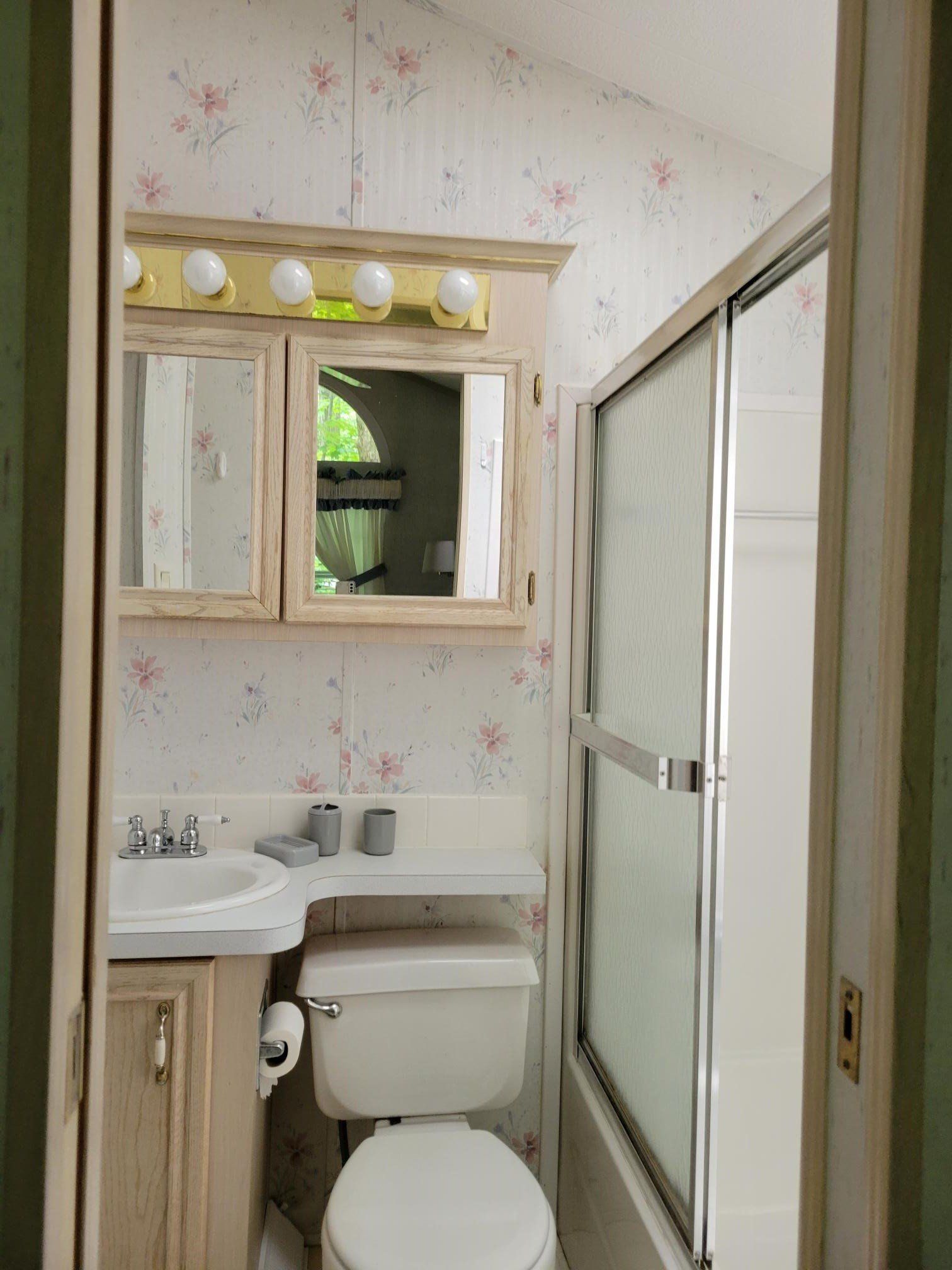 Small bathroom with sink, toilet, shower stall, and a vanity mirror with lights.