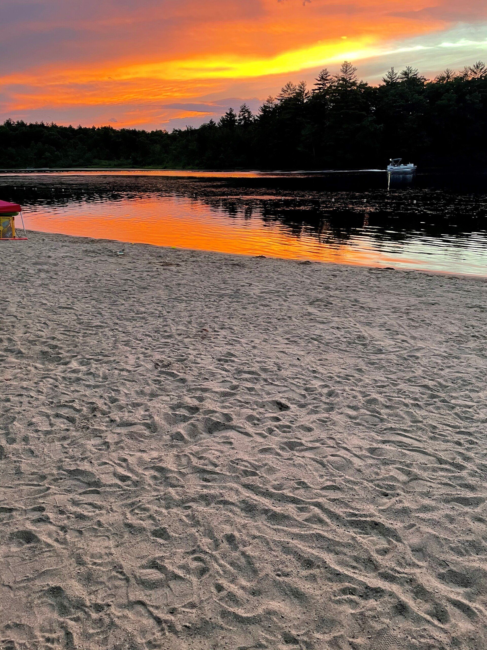 Sunset over a calm lake with orange clouds reflecting on the water beside a sandy shore