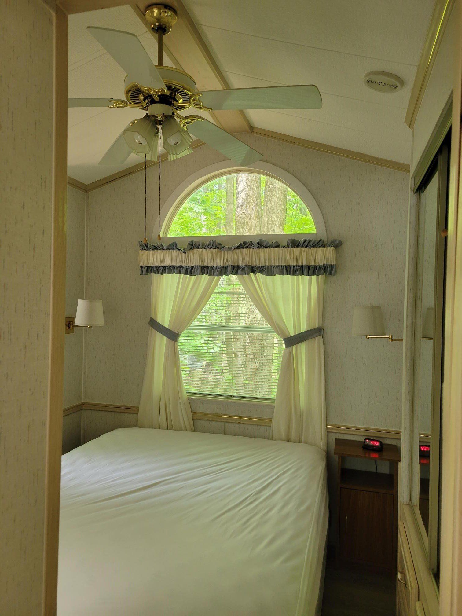 Small bedroom with arched window, bed, ceiling fan, and light curtains
