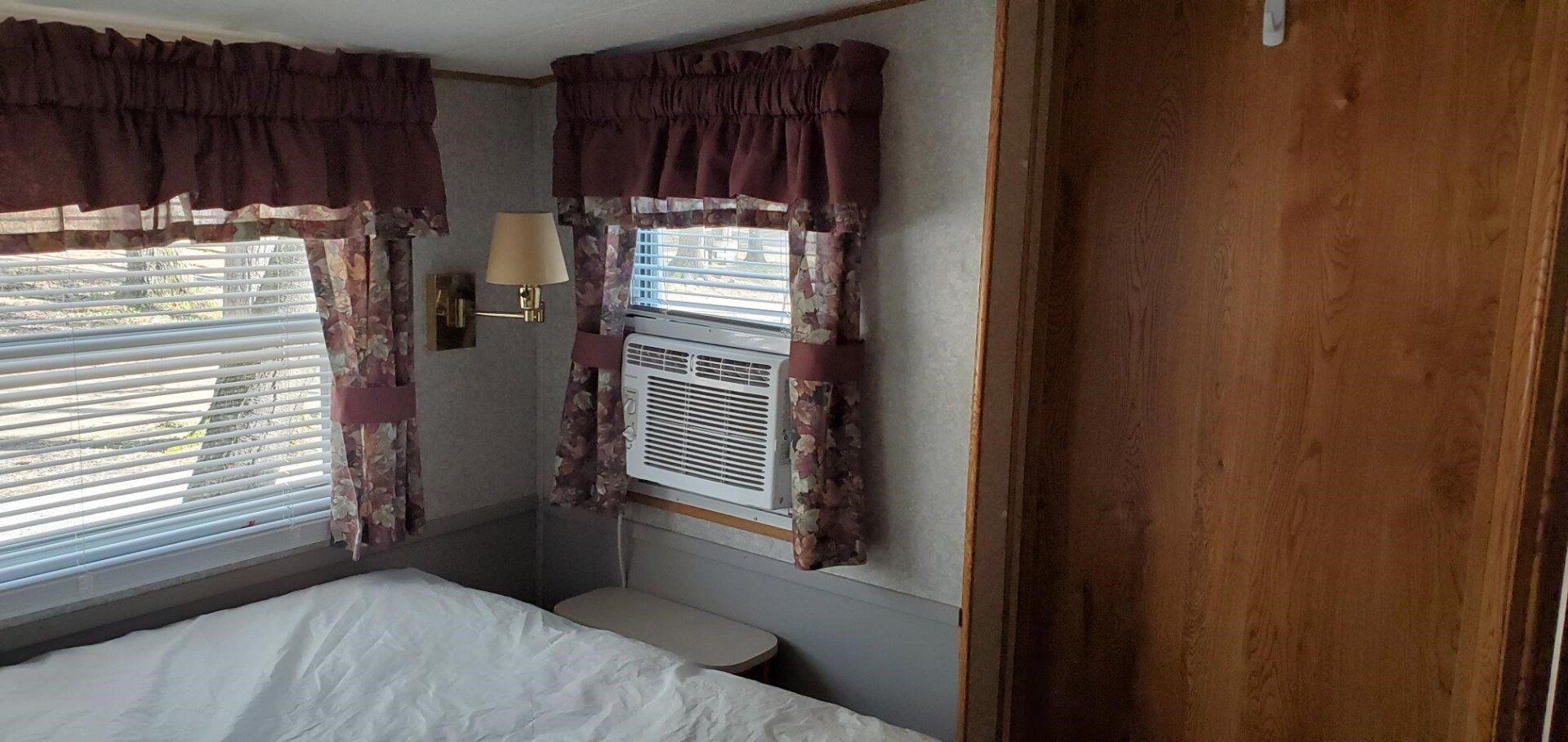 Cozy bedroom corner with two windows, red curtains, a bed, and wood-paneled walls