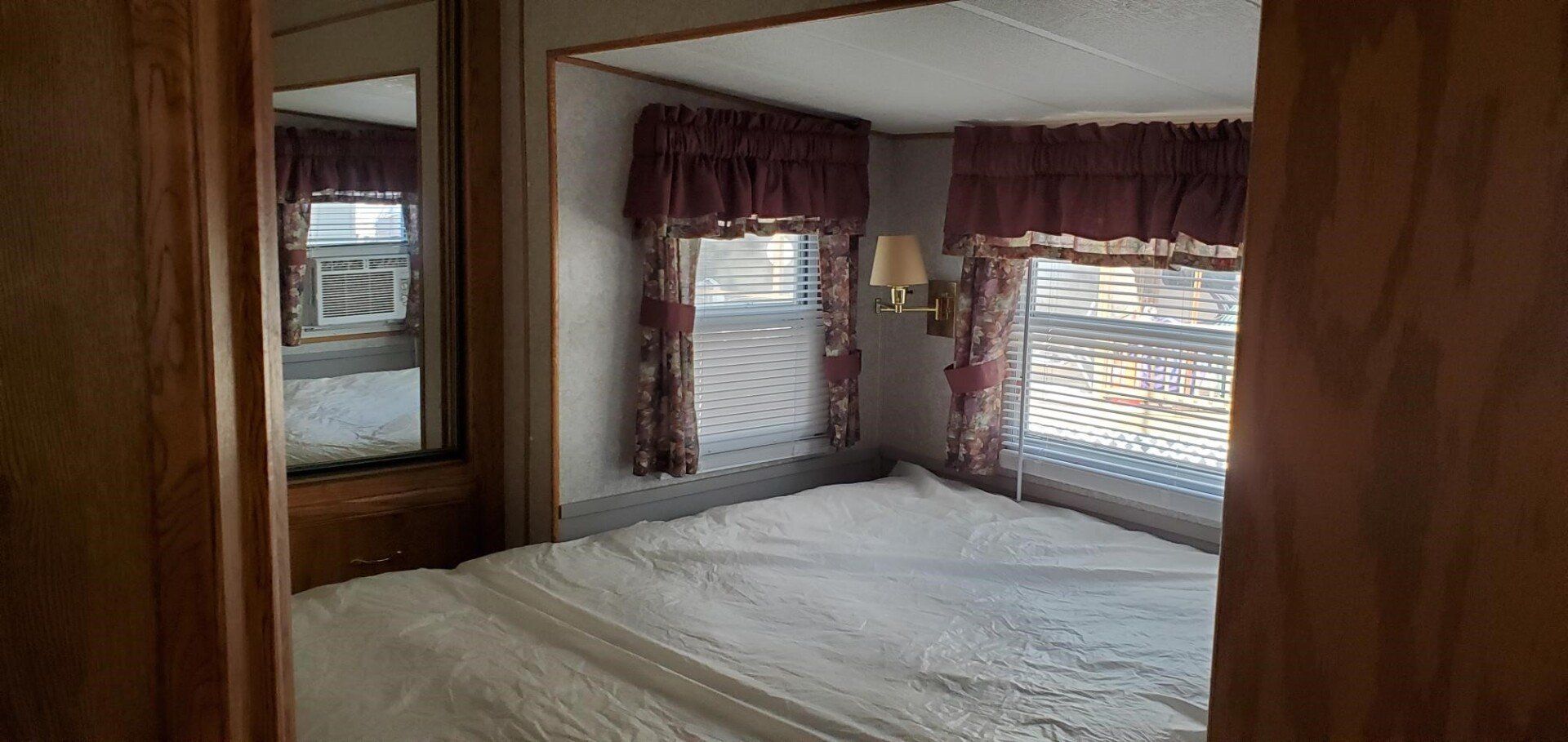 Wood-paneled bedroom with a bed, curtained windows, and daylight filtering through blinds.