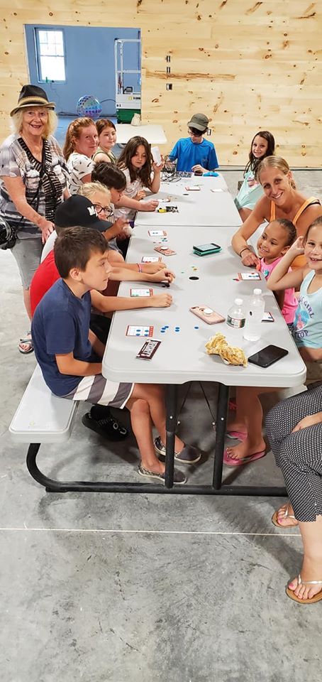 Group of people seated around a long white table in a bright indoor room, sharing a meal and smiling.