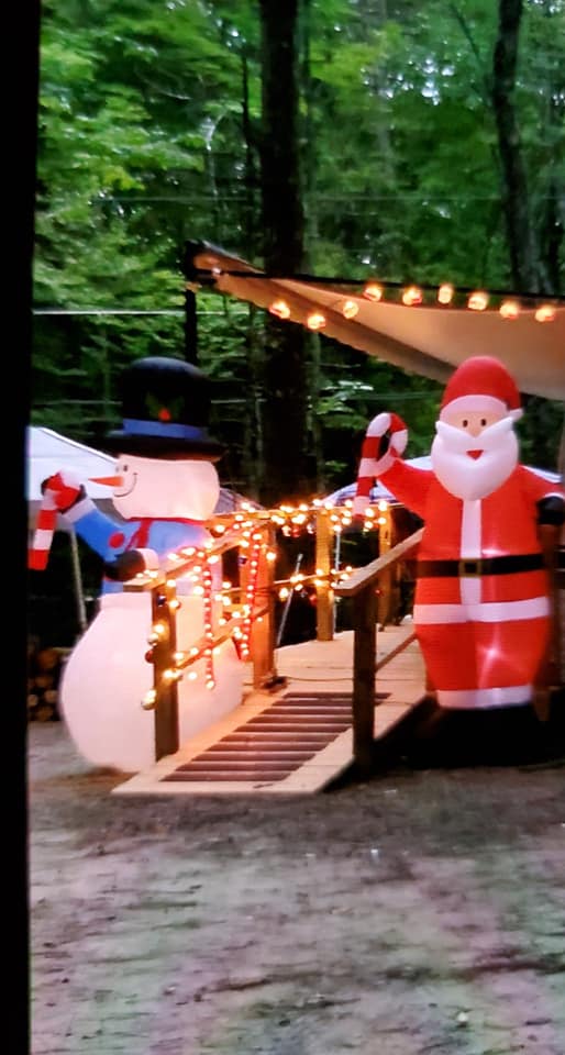 Christmas lights and Santa decorations beside a small wooden bridge in a wooded area