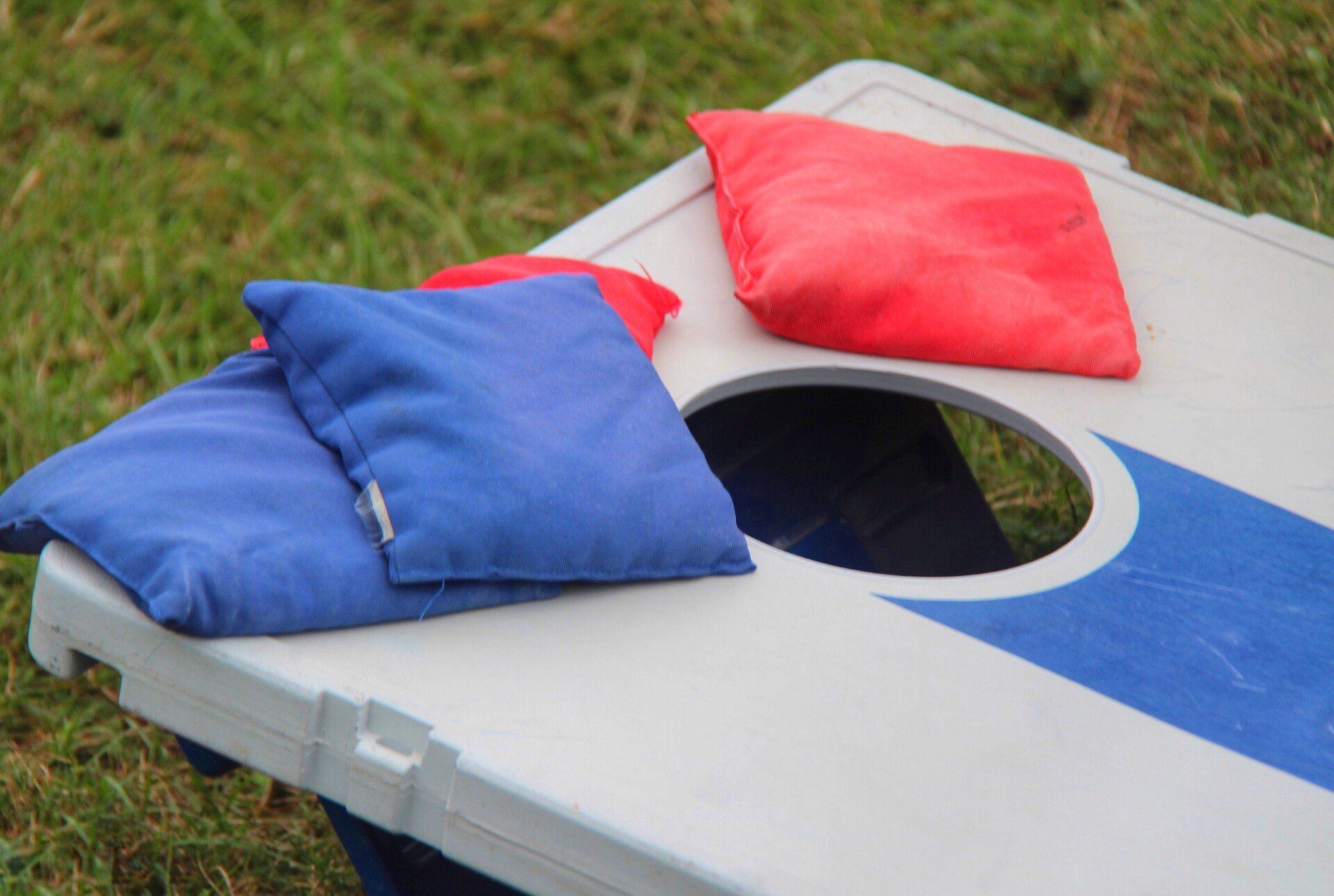 Blue and red bean bags on a white cornhole board outdoors on grass