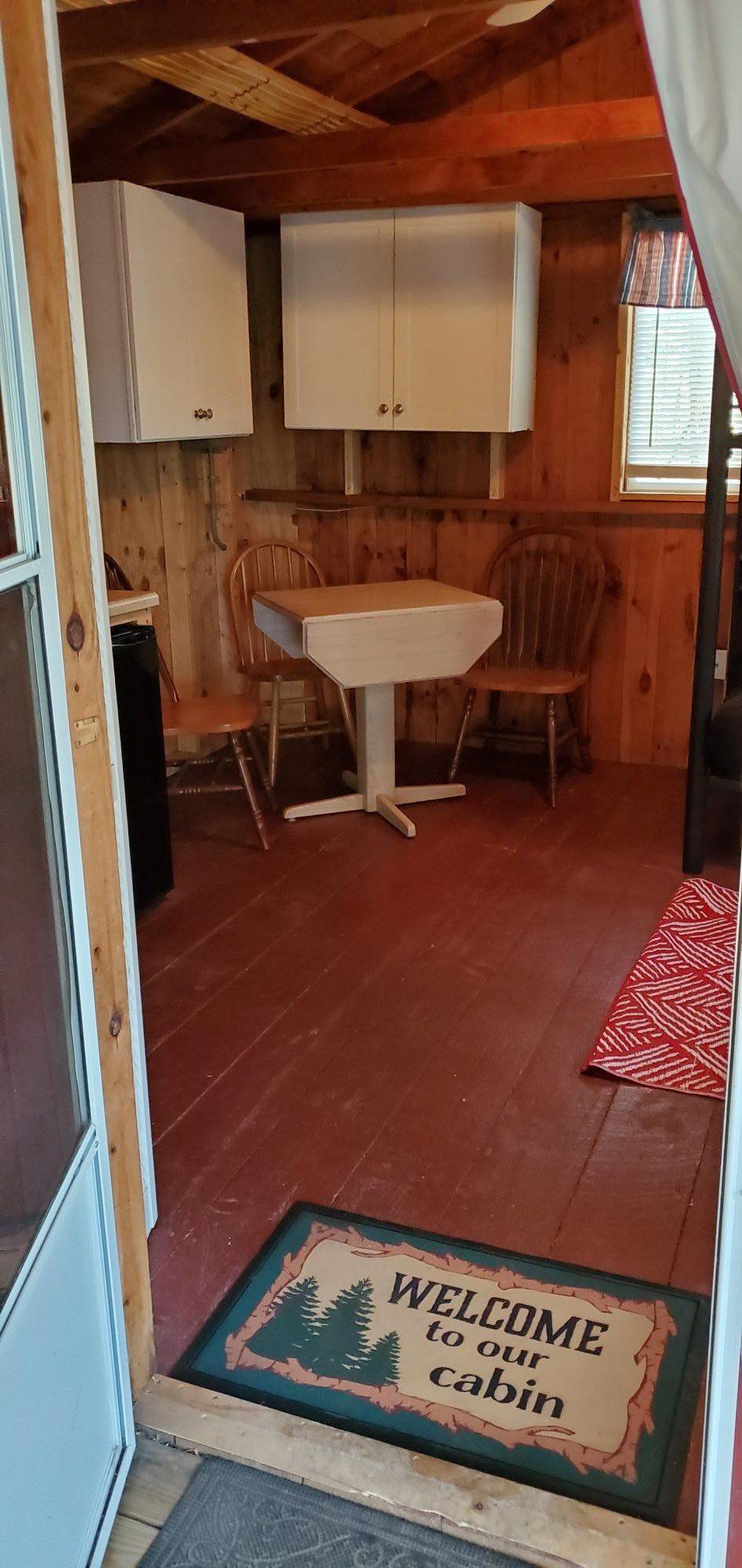 Small rustic cabin bathroom with white sink, wooden walls, and a welcome mat on the floor.
