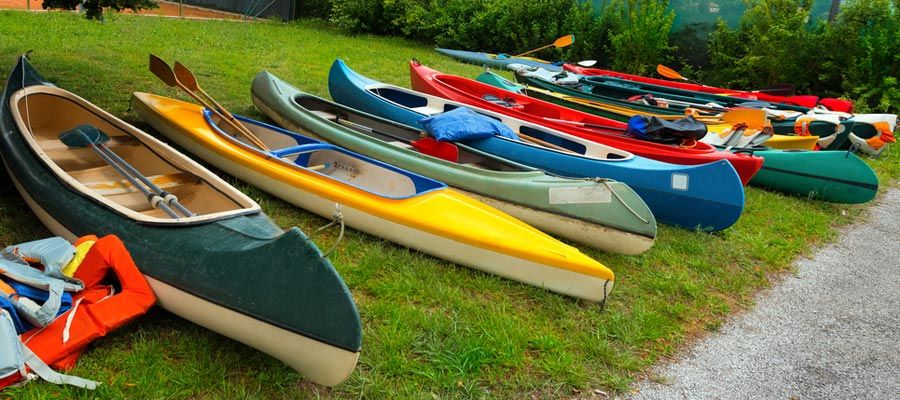 Several colorful kayaks and canoes lined up on grass beside a gravel path