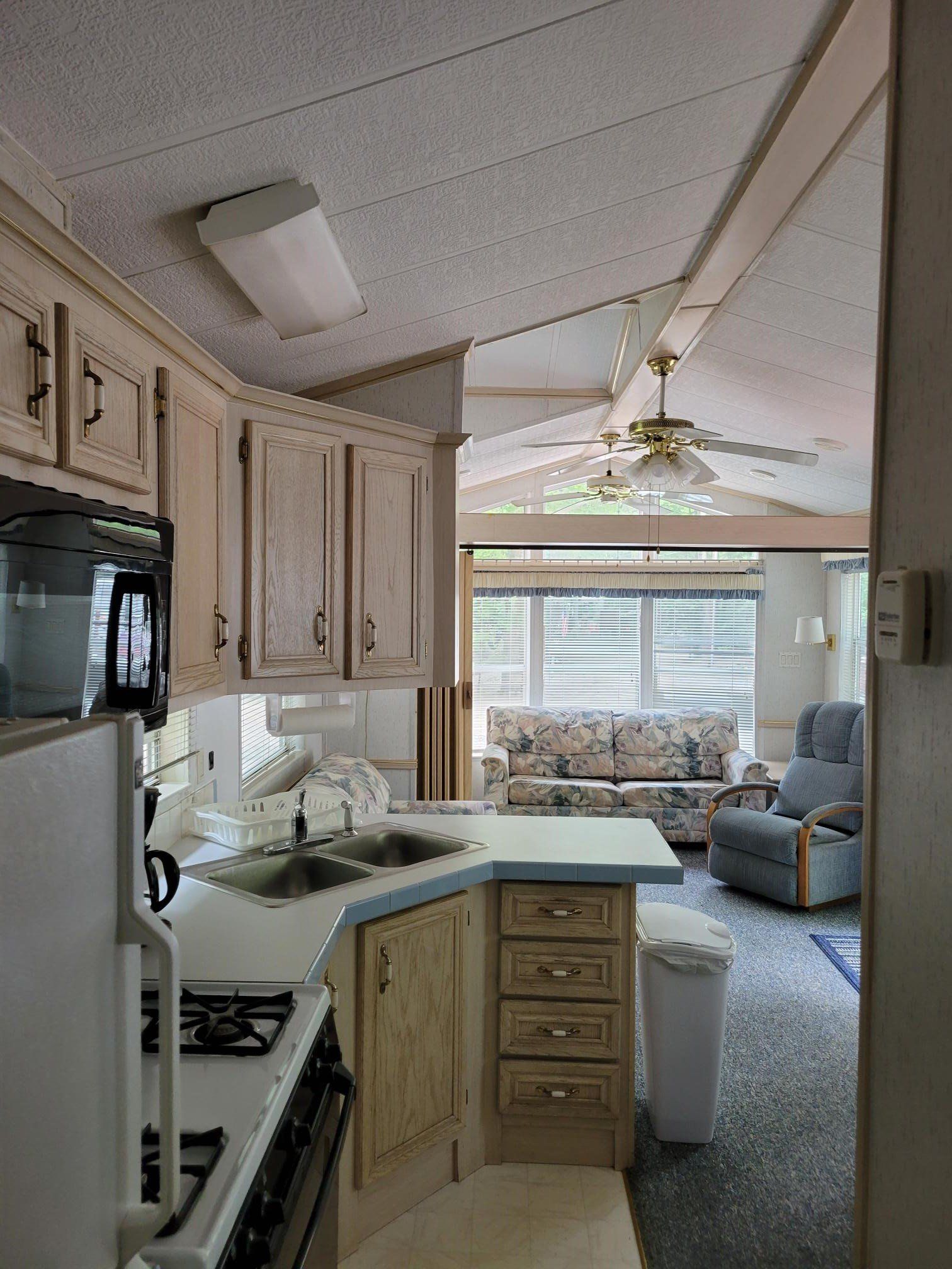 Compact kitchen with light wood cabinets, white counters, and a view into a cozy living room.