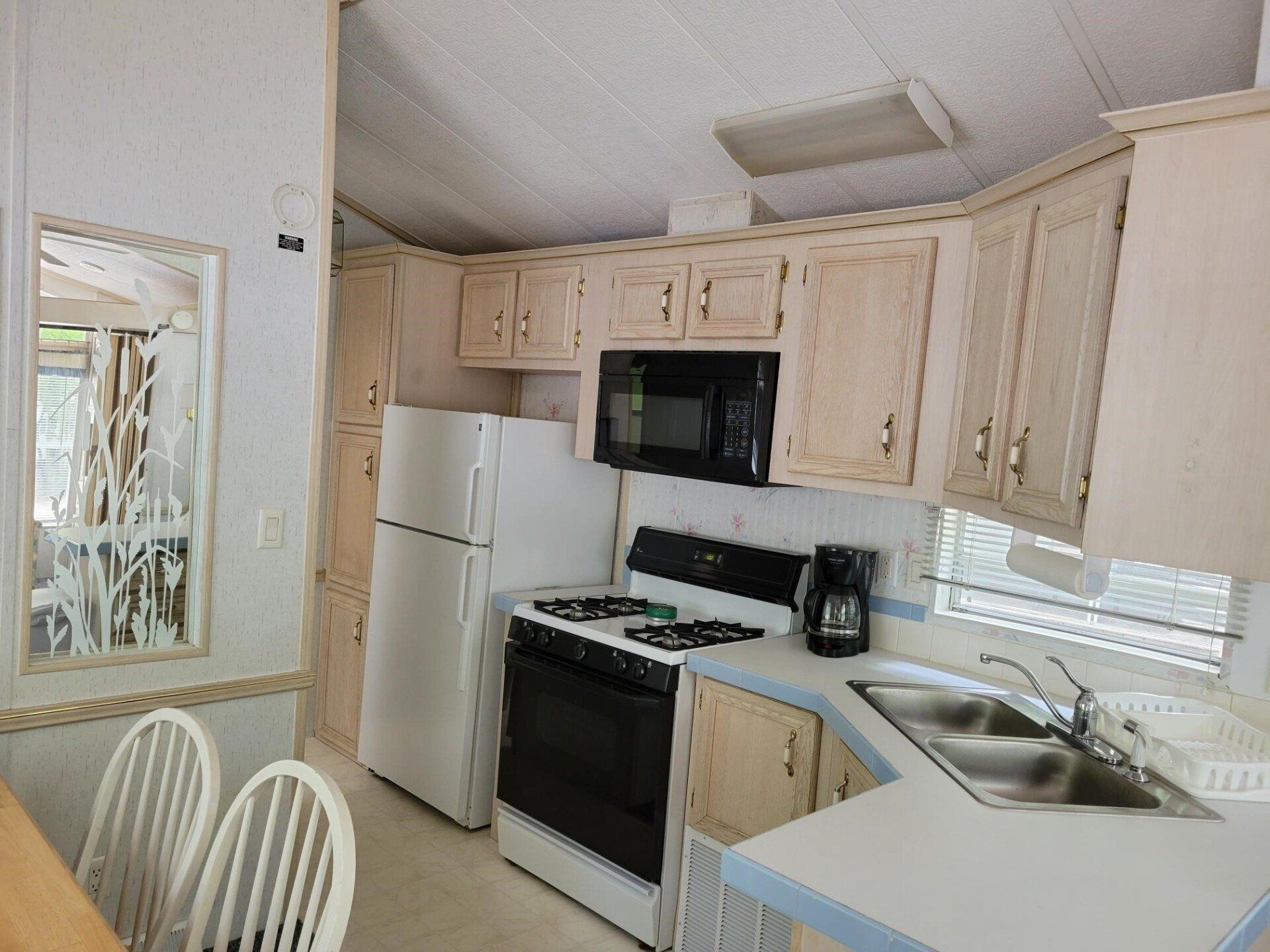 Bright kitchen with white cabinets, white stove and fridge, beige walls, and a sink by a window.