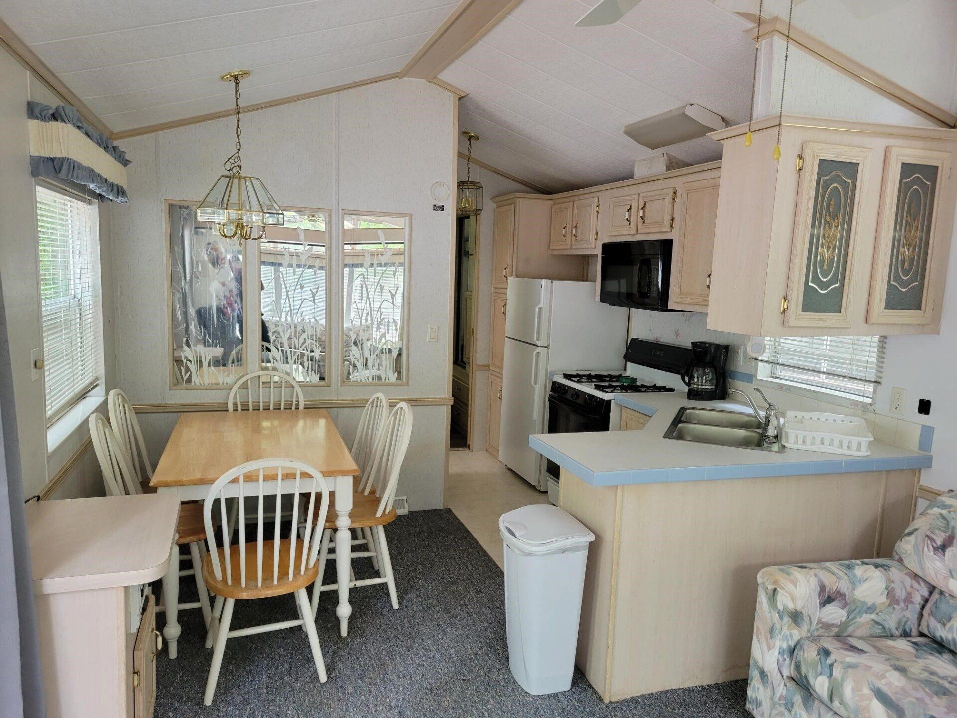 Small kitchen and dining nook with light wood cabinets, white appliances, table, and floral chair.