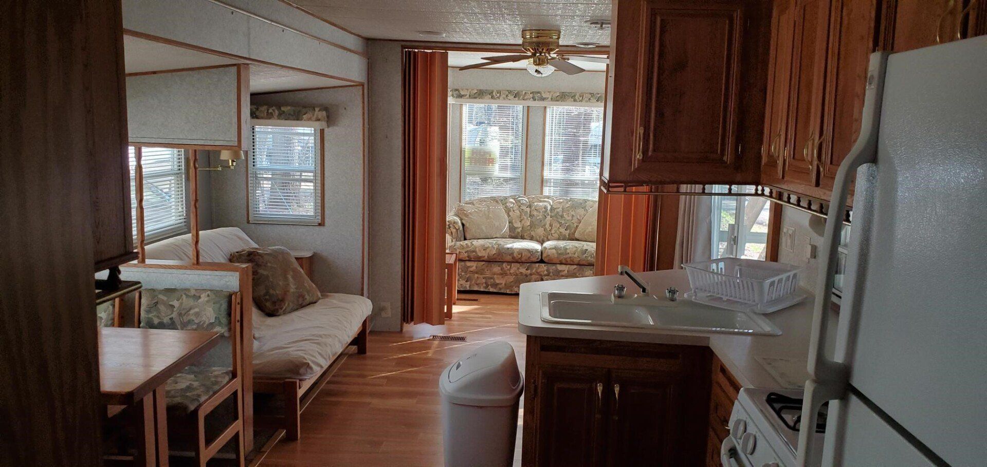 Cozy kitchen-living room with wood cabinets, white appliances, sofa, and large windows overlooking a lake.