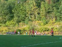 Soccer players in red on a grassy field near a forested hillside