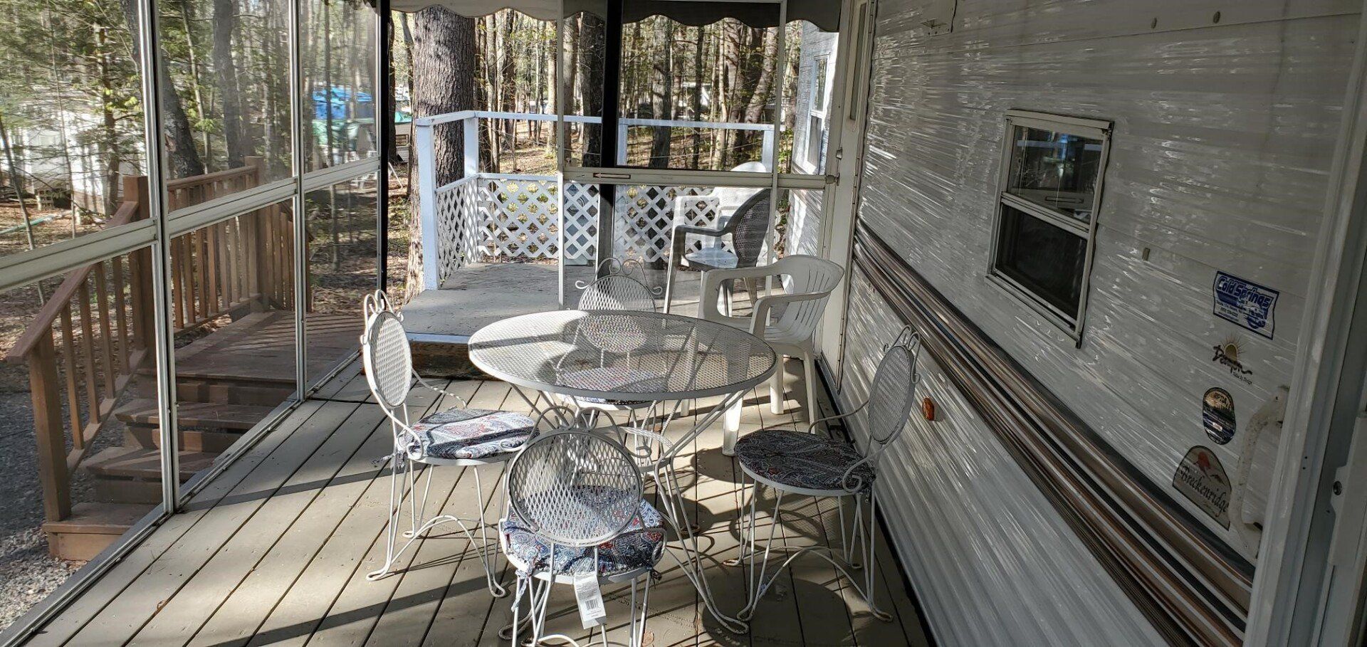White metal patio table and chairs on a screened porch beside a trailer wall and railing.
