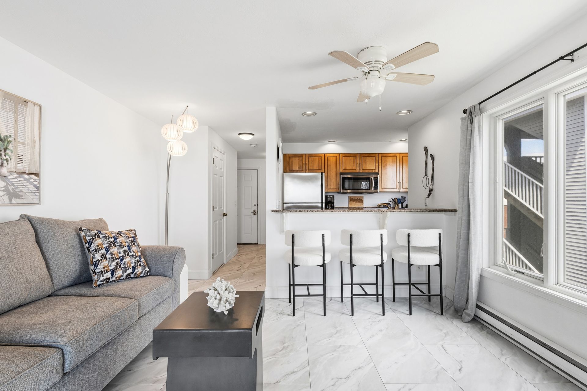 Bright living room with beige sectional, white coffee table, and open kitchen in the background