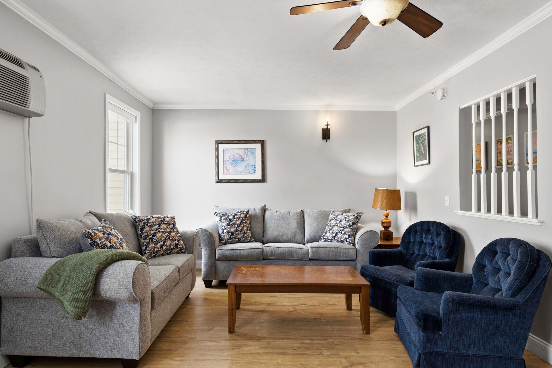 Bright living room with gray sofa, blue chairs, wooden coffee table, and ceiling fan