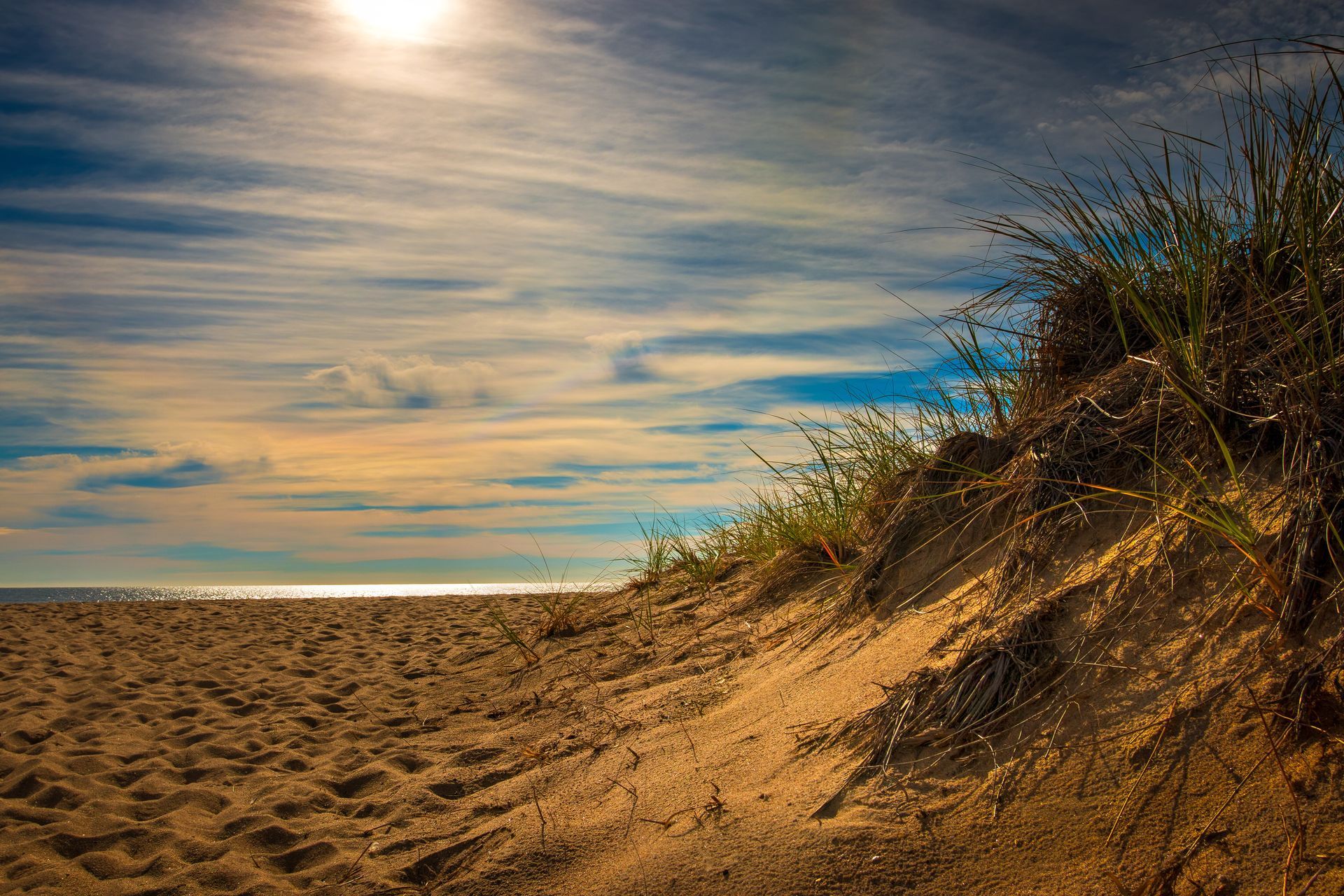 A sand dune on a beach with the sun shining through the clouds.