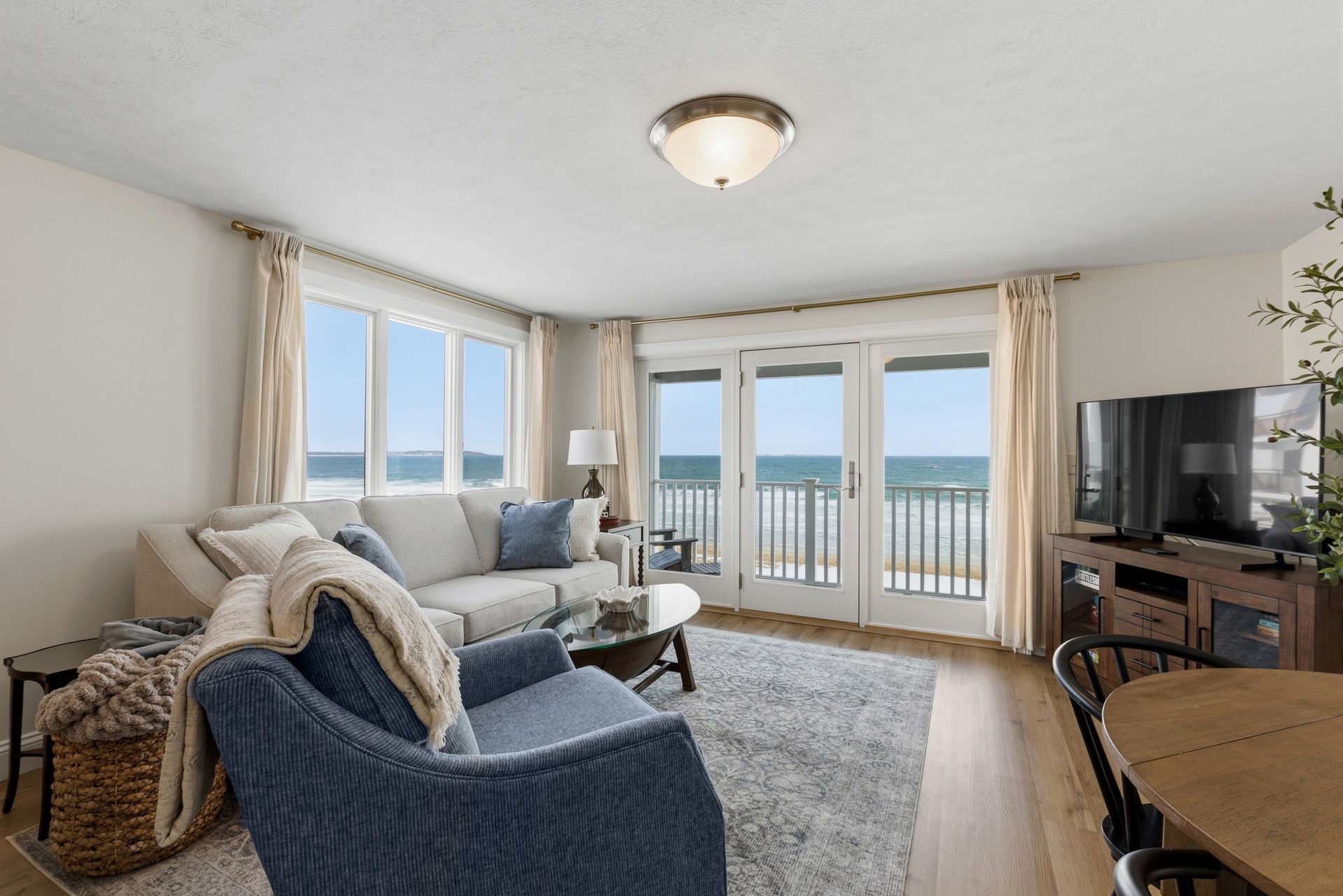 Living room with ocean view, featuring a couch, blue chair, rug, and TV.