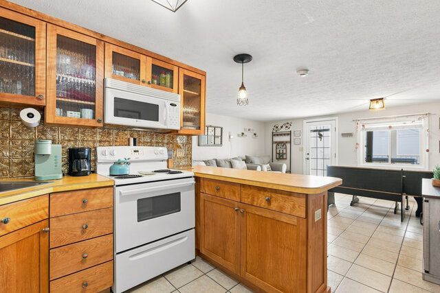 Bright kitchen with wood cabinets, white stove and microwave, island, and dining area in the background