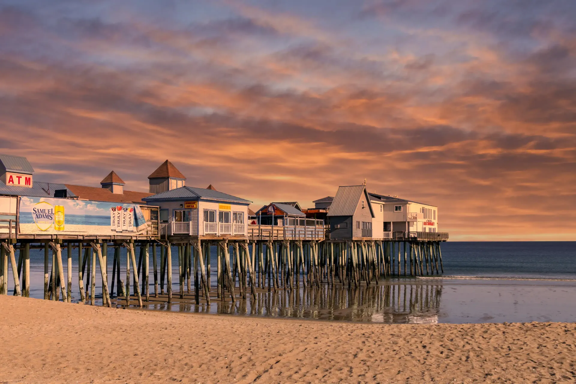 A pier on a beach with a sunset in the background