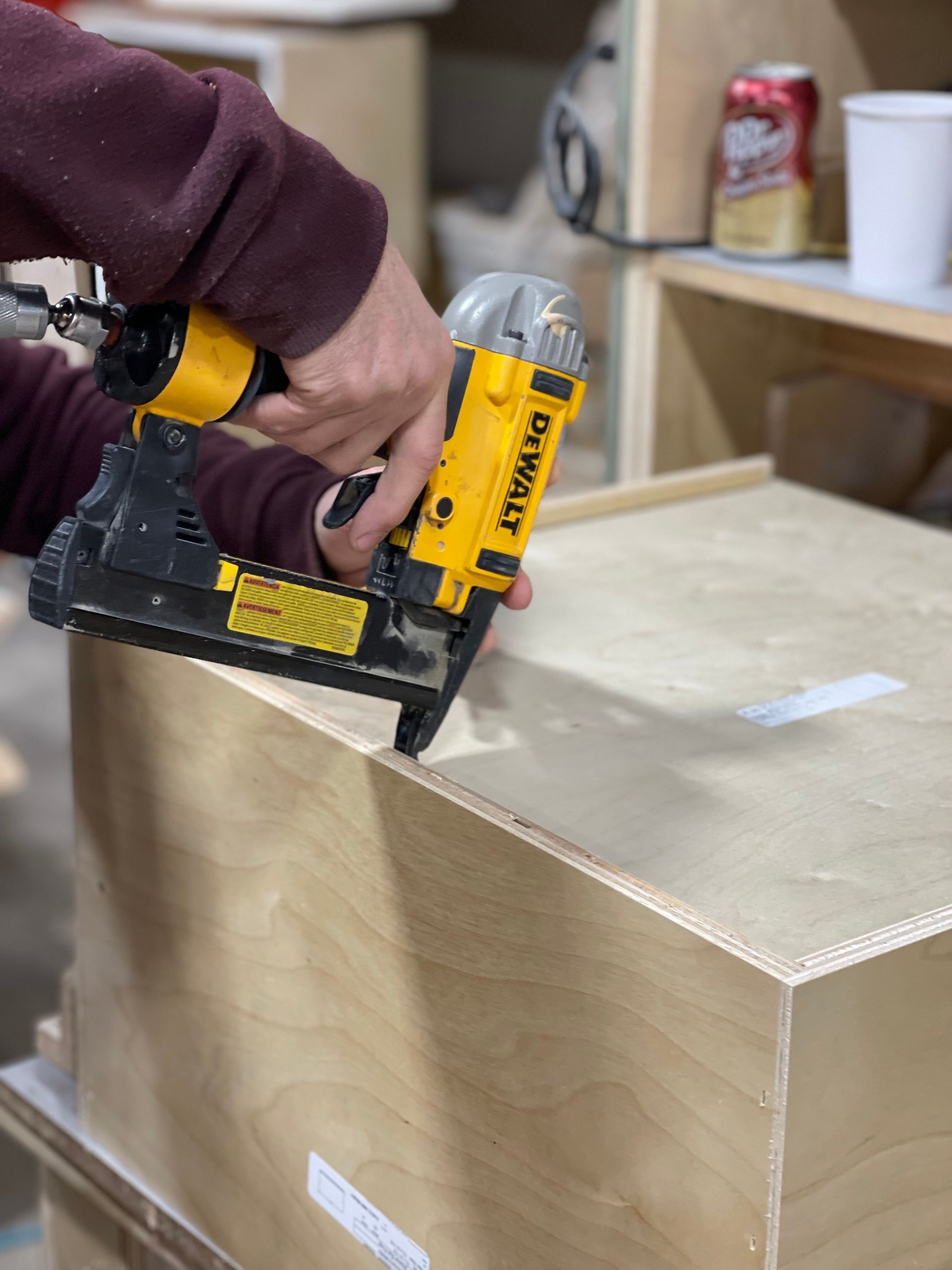 Person uses a yellow and black nail gun to assemble a wooden box in a workshop.
