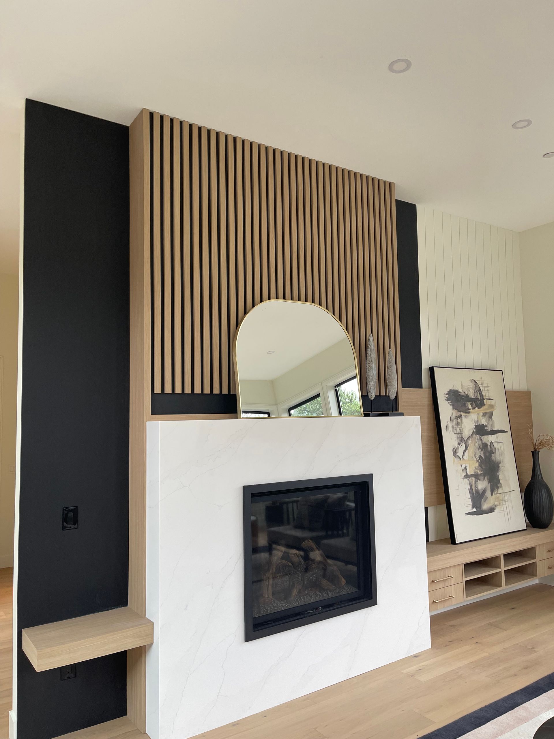 A fireplace feature wall with wood slats, a marble surround, an arched mirror, and black accent walls.