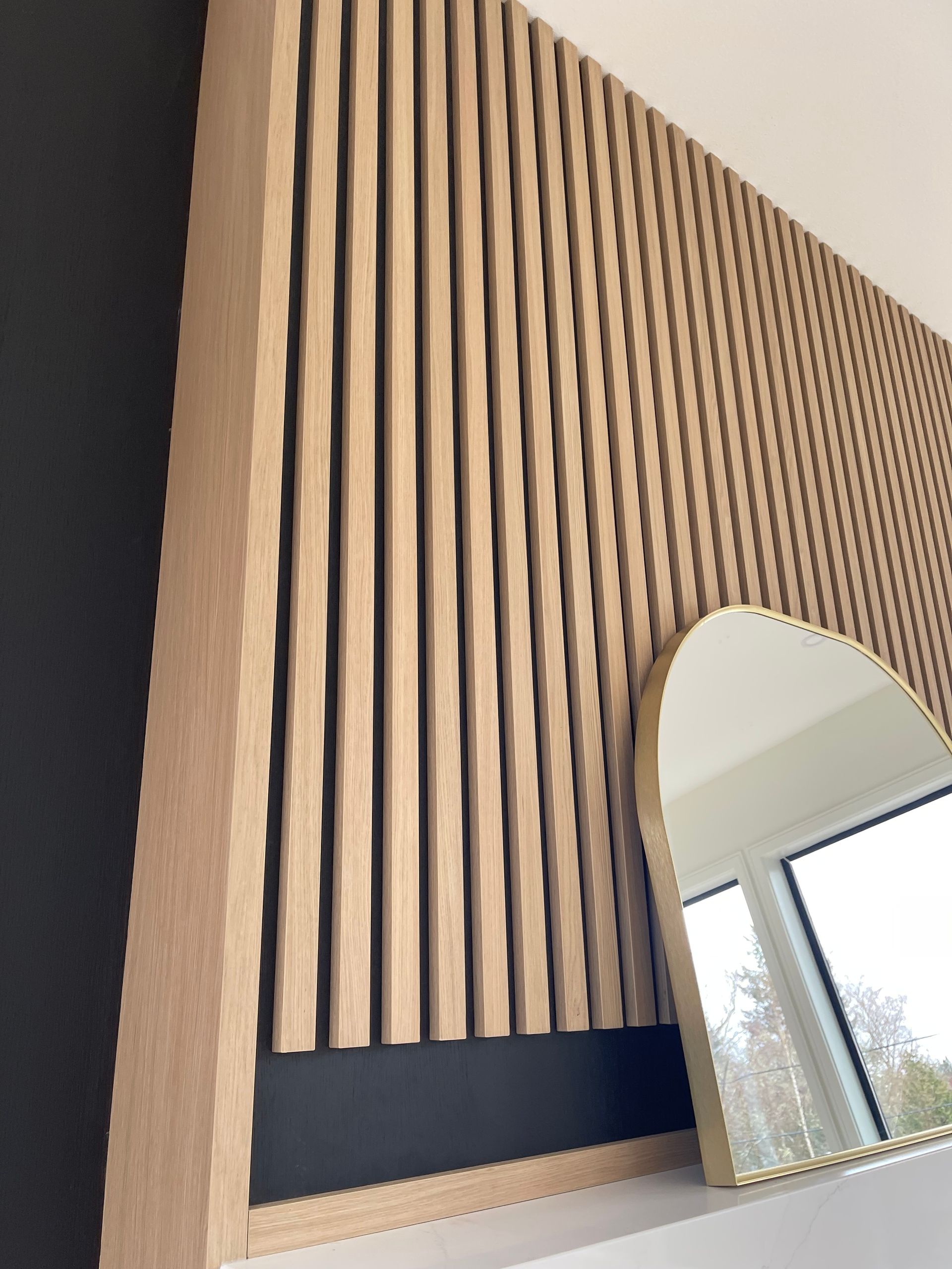 Vertical wood slat wall with a round mirror and large window in a modern interior