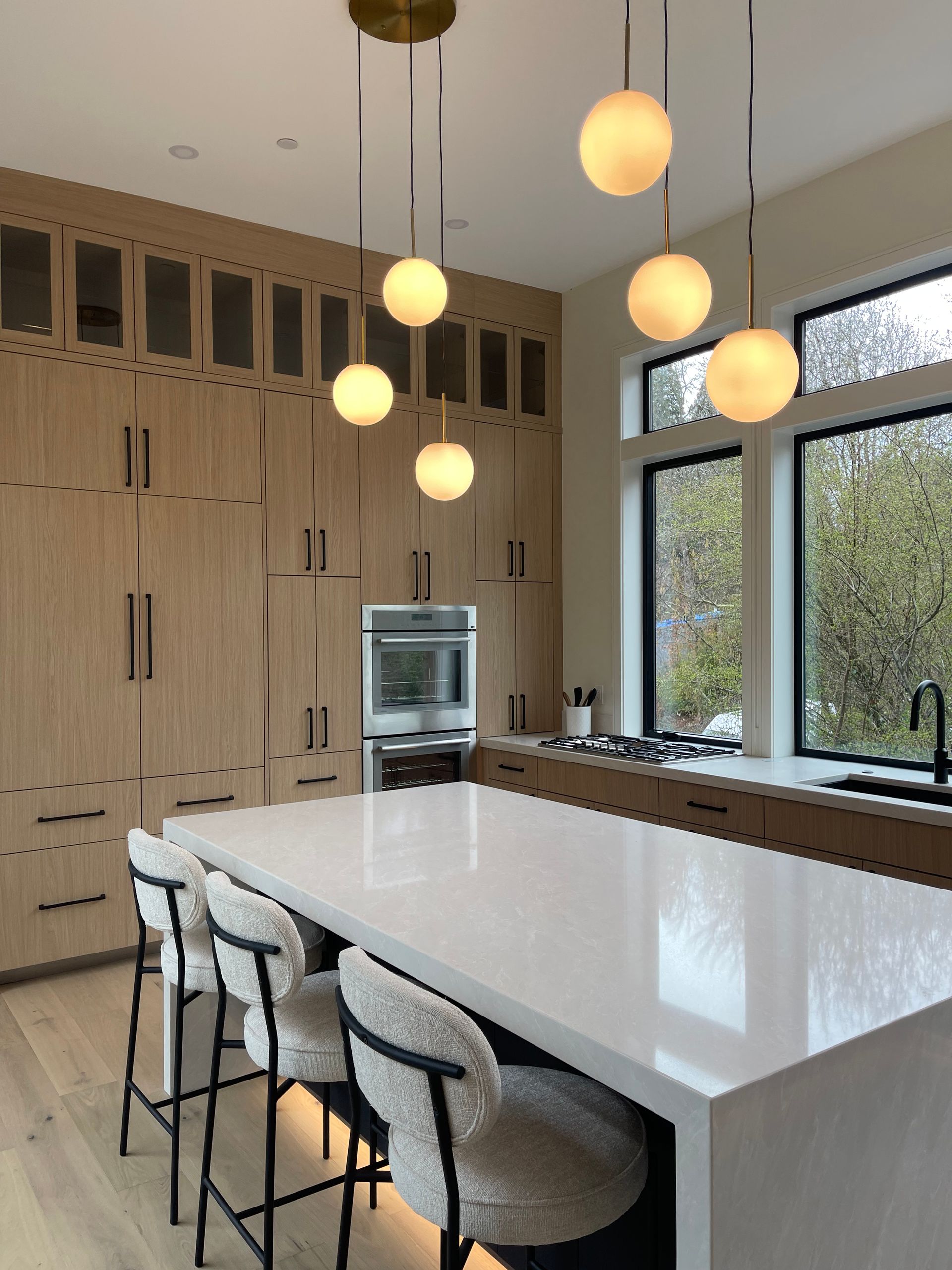 Modern kitchen in Portland with a large white island, textured stools, light wood cabinetry. Pro-tech woodworking in Portland