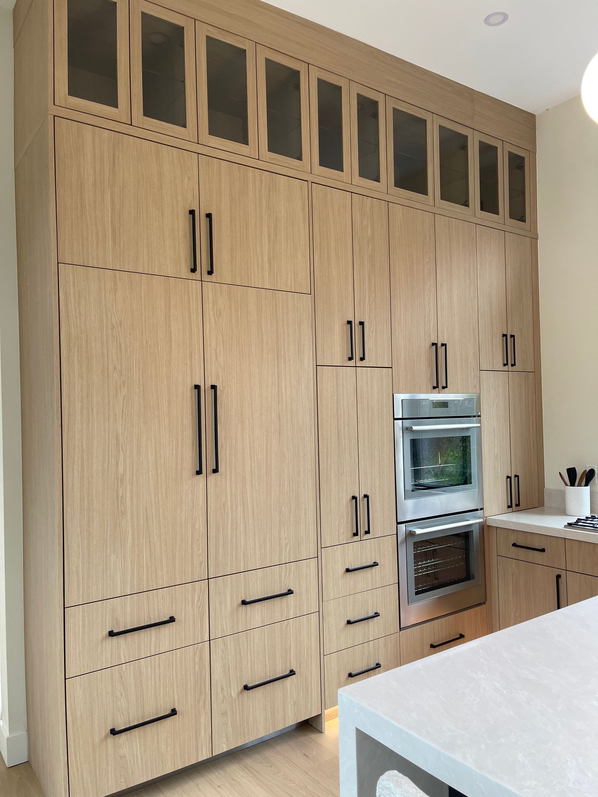 A wall of floor-to-ceiling light oak cabinetry with matte black handles. Pro-tech woodworking in Portland