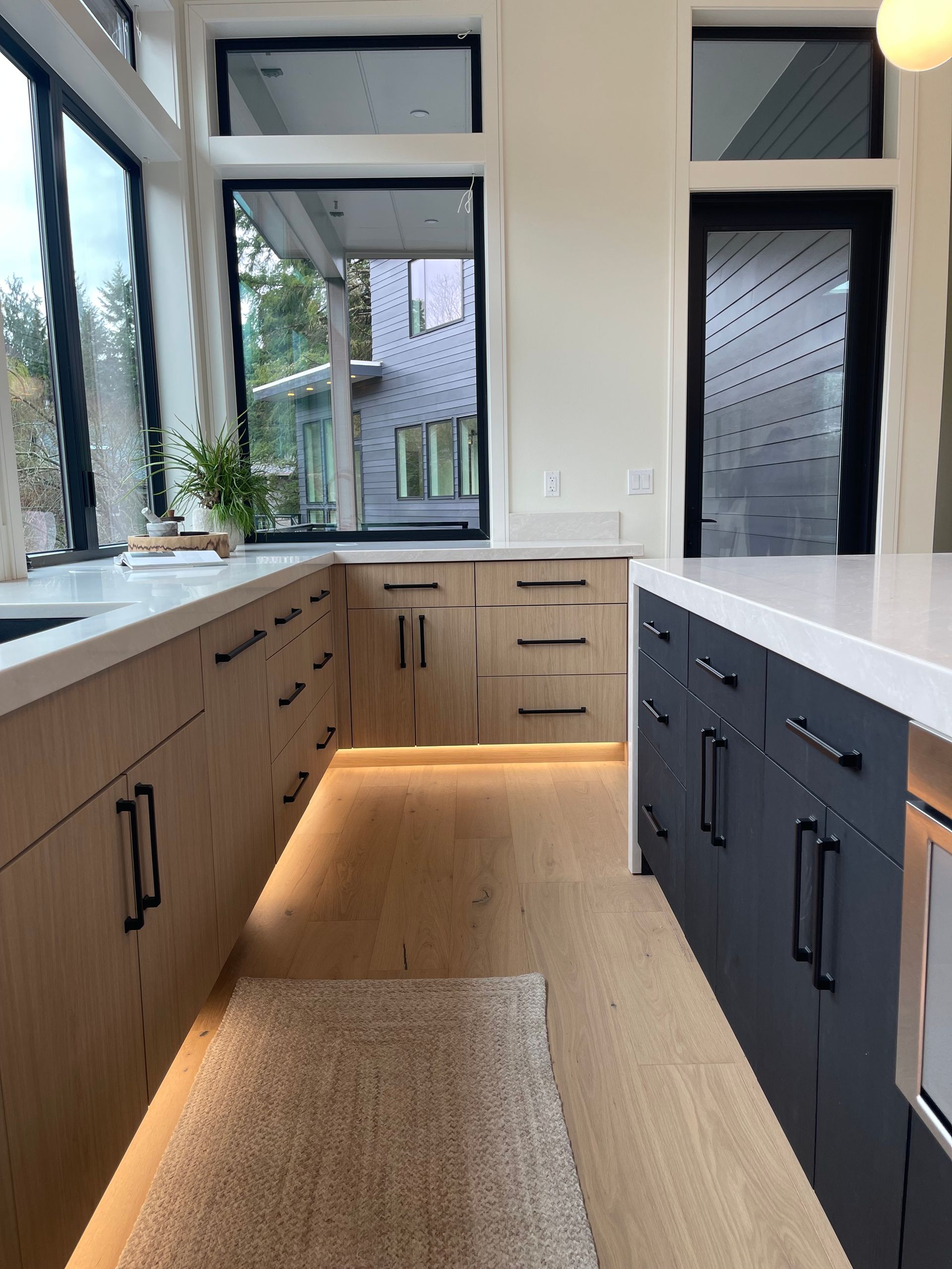 A modern kitchen with light wood lower cabinets, black island cabinets, white countertops. Pro-tech woodworking in Portland
