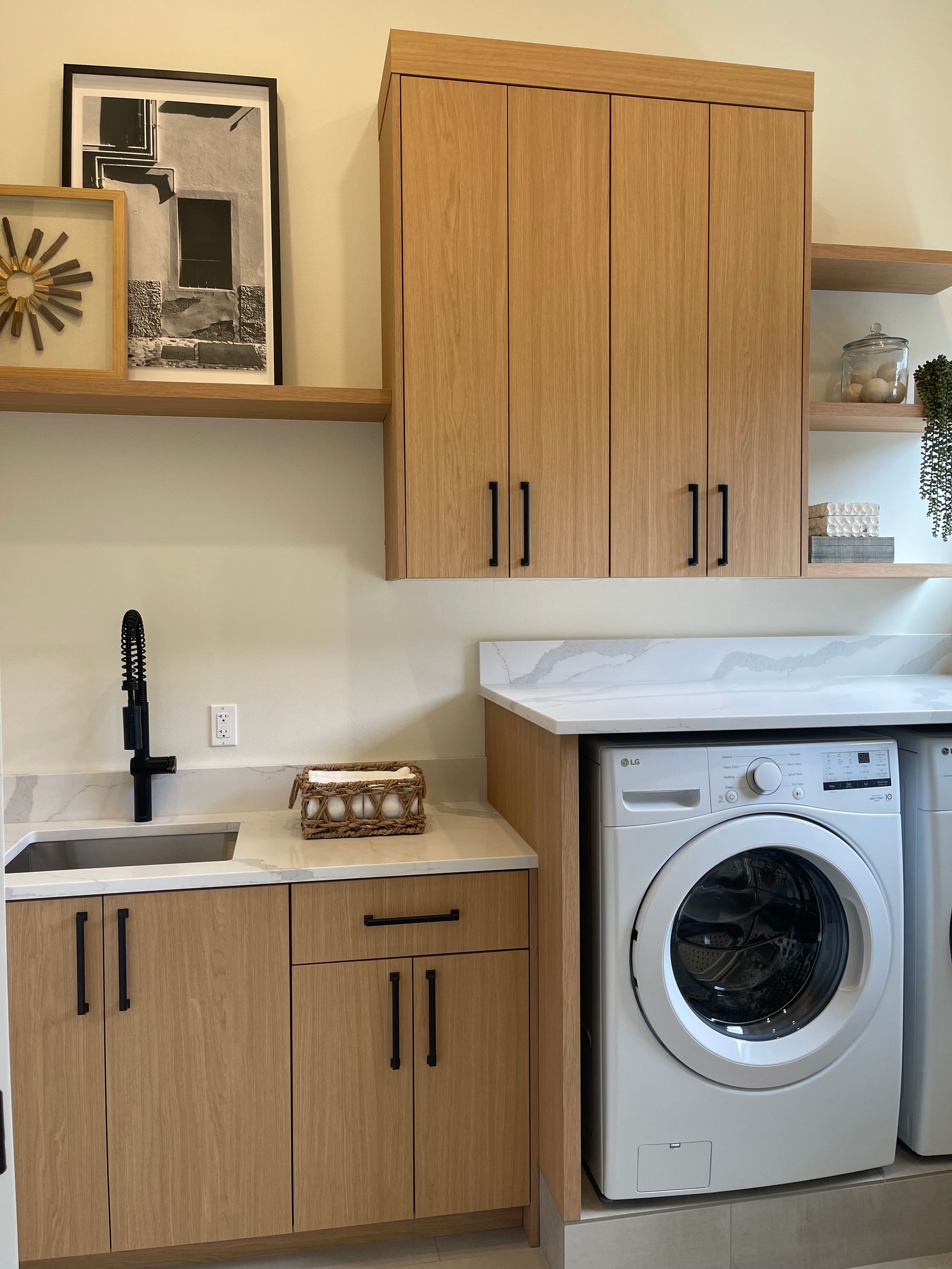 A laundry room with oak cabinets, light countertops, a black sink faucet, and a white front-loading washing machine.