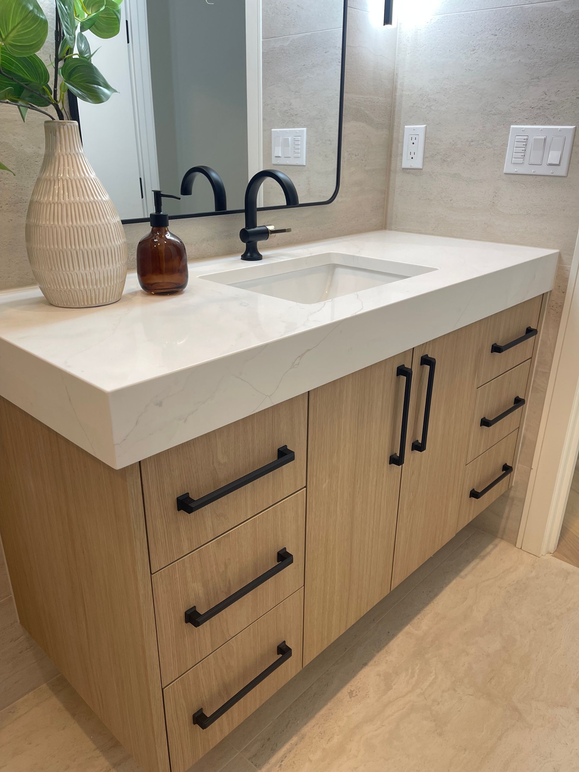 Modern bathroom vanity with light wood cabinets, black hardware, a white quartz countertop, and a black-framed mirror.