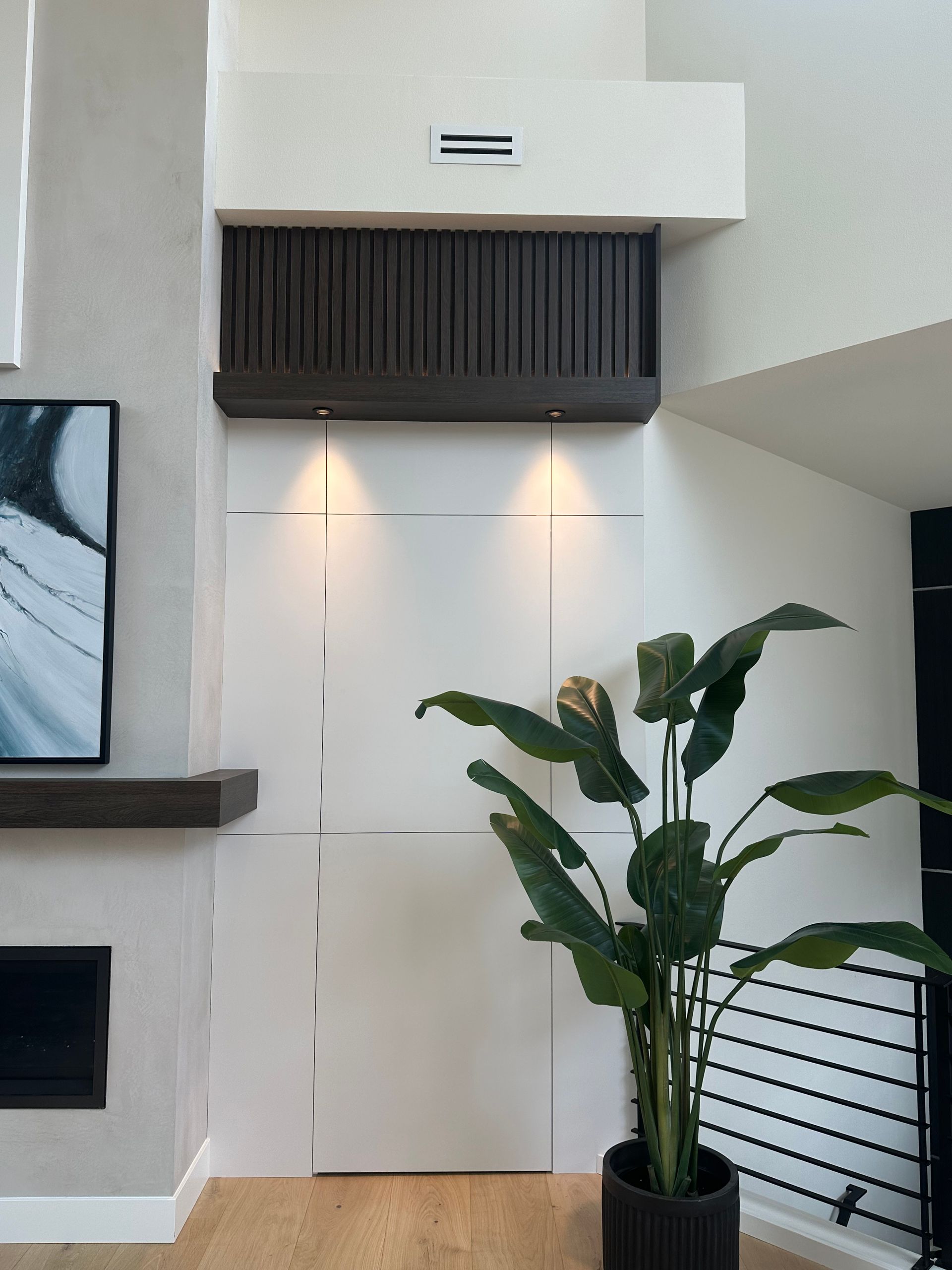 Modern interior wall with a black vent, warm accent lights, and a potted plant beside a stair railing