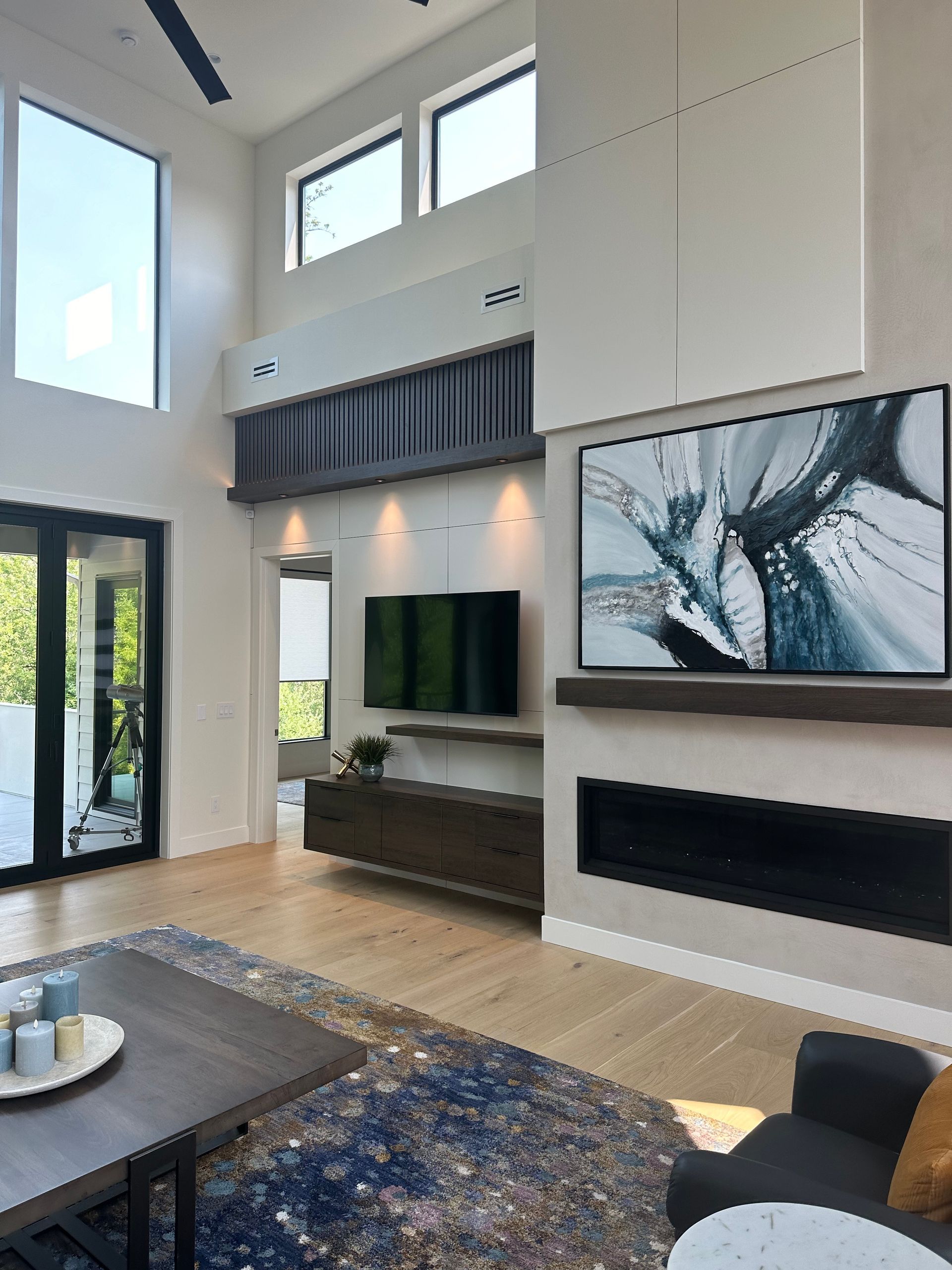 Modern living room with high ceilings, fireplace, large TV, and wooden floor.