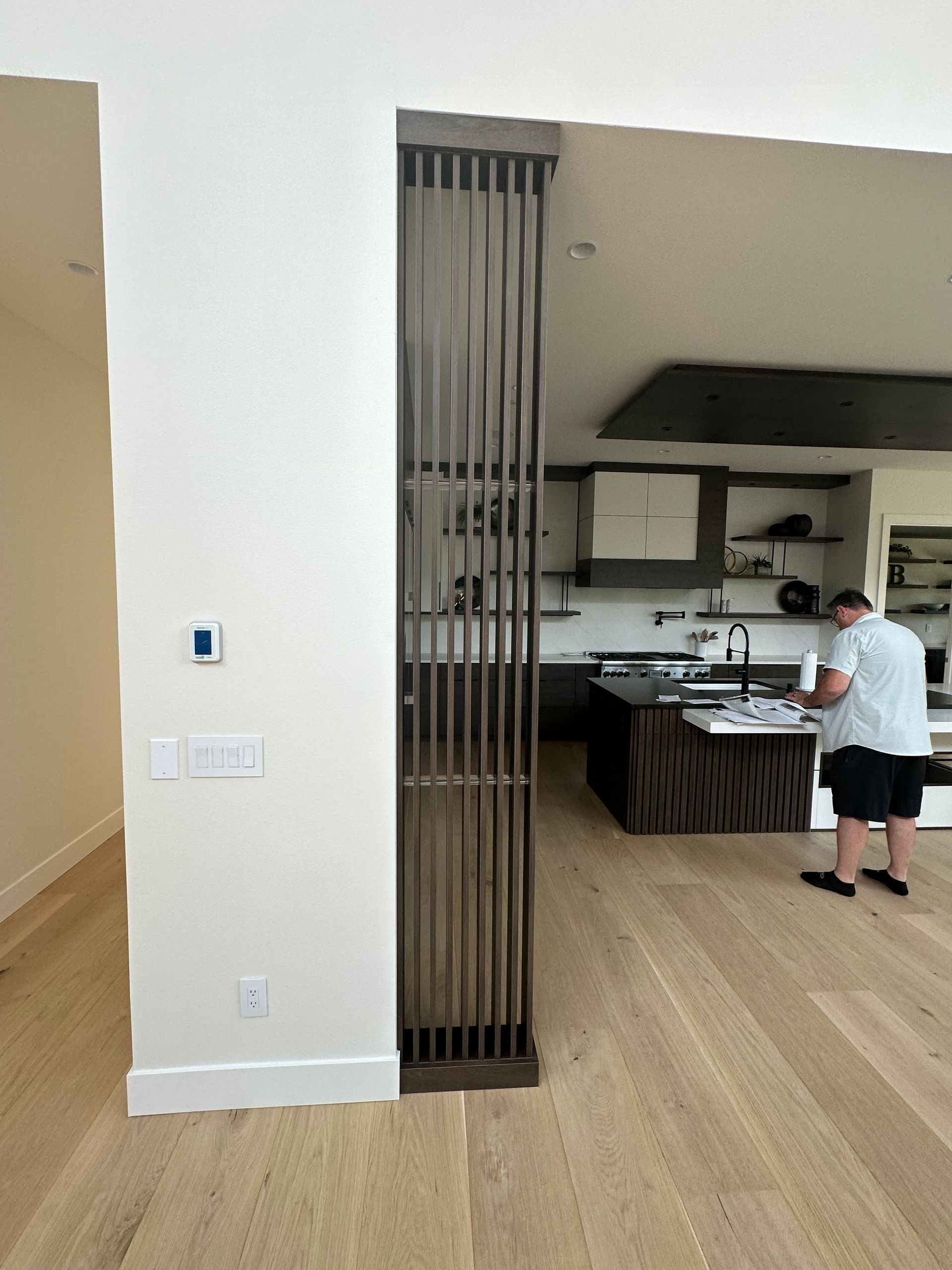 Modern kitchen with wood flooring, dark cabinetry, and a person standing near the island