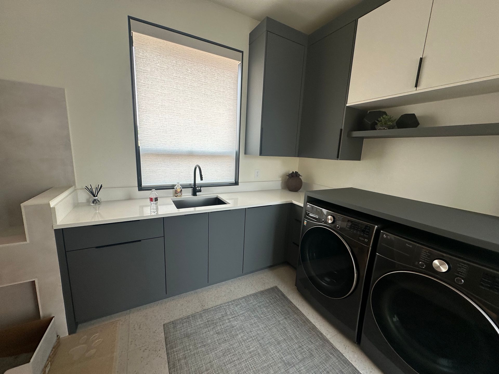 Laundry room with gray cabinets, white countertop, black sink, and a washer/dryer set.