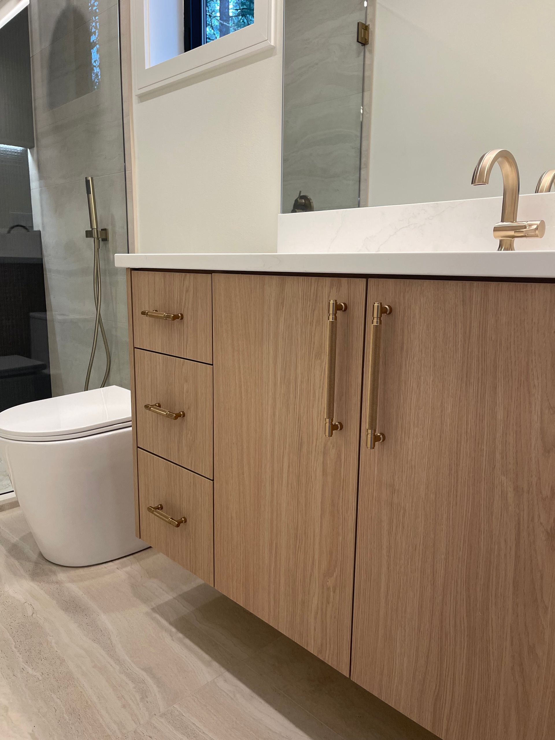 Modern bathroom featuring a light wood vanity with gold hardware, a white countertop, and a white toilet.