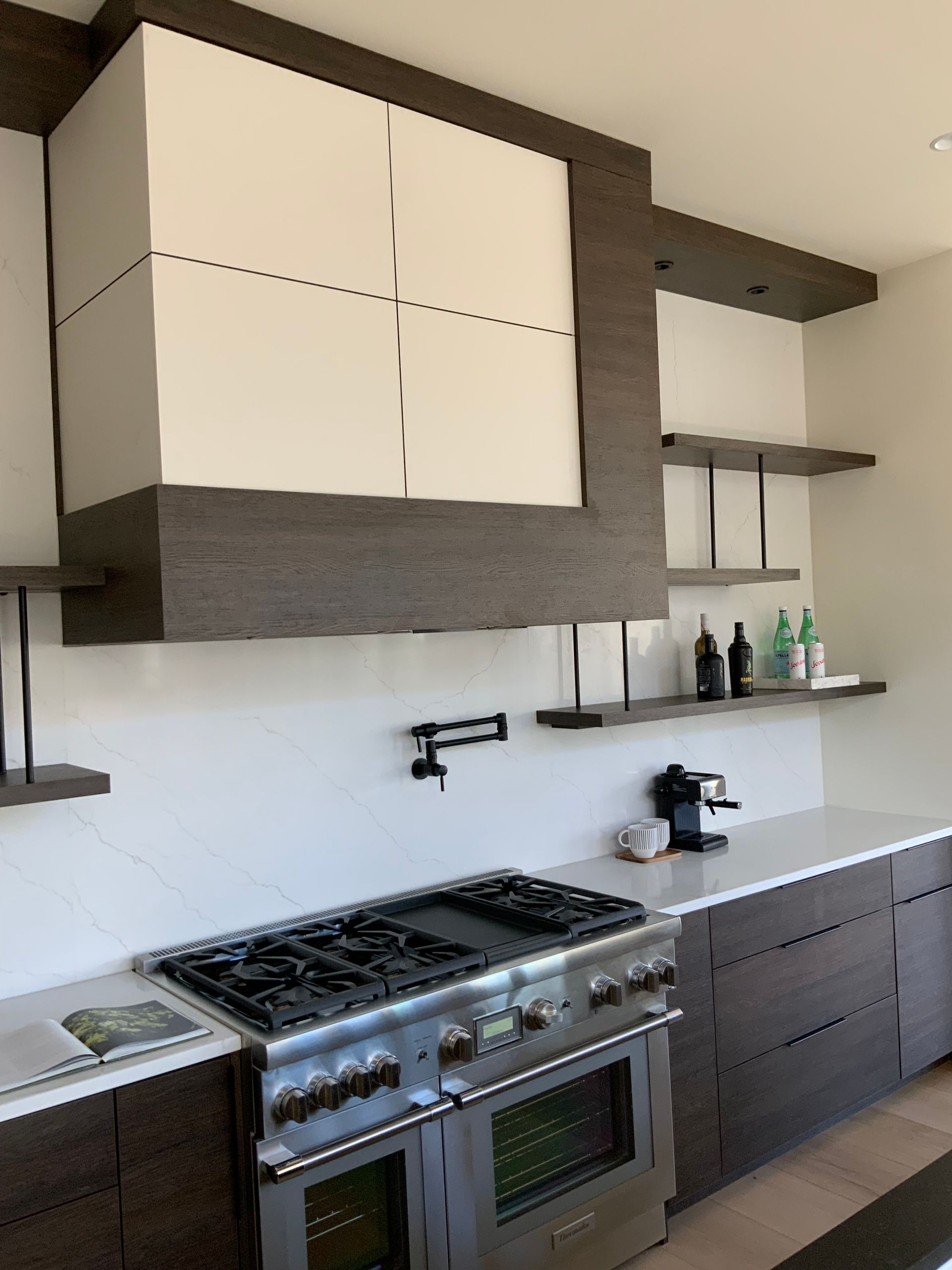 Modern kitchen with dark wood cabinets, stainless steel range, and white countertops.