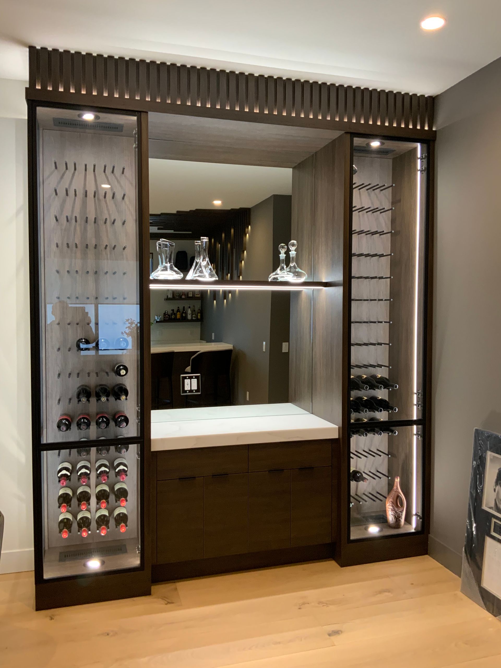 Wine display cabinet with glass doors, bottle racks, and ambient lighting, reflecting a bar area.