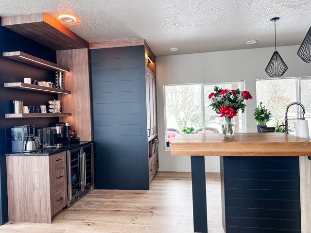 Modern kitchen with dark blue and wood cabinetry, island with butcher block top, and a coffee station.