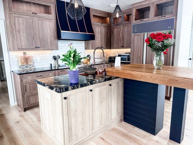 Kitchen with light wood cabinets, dark blue range hood, and black island countertop.