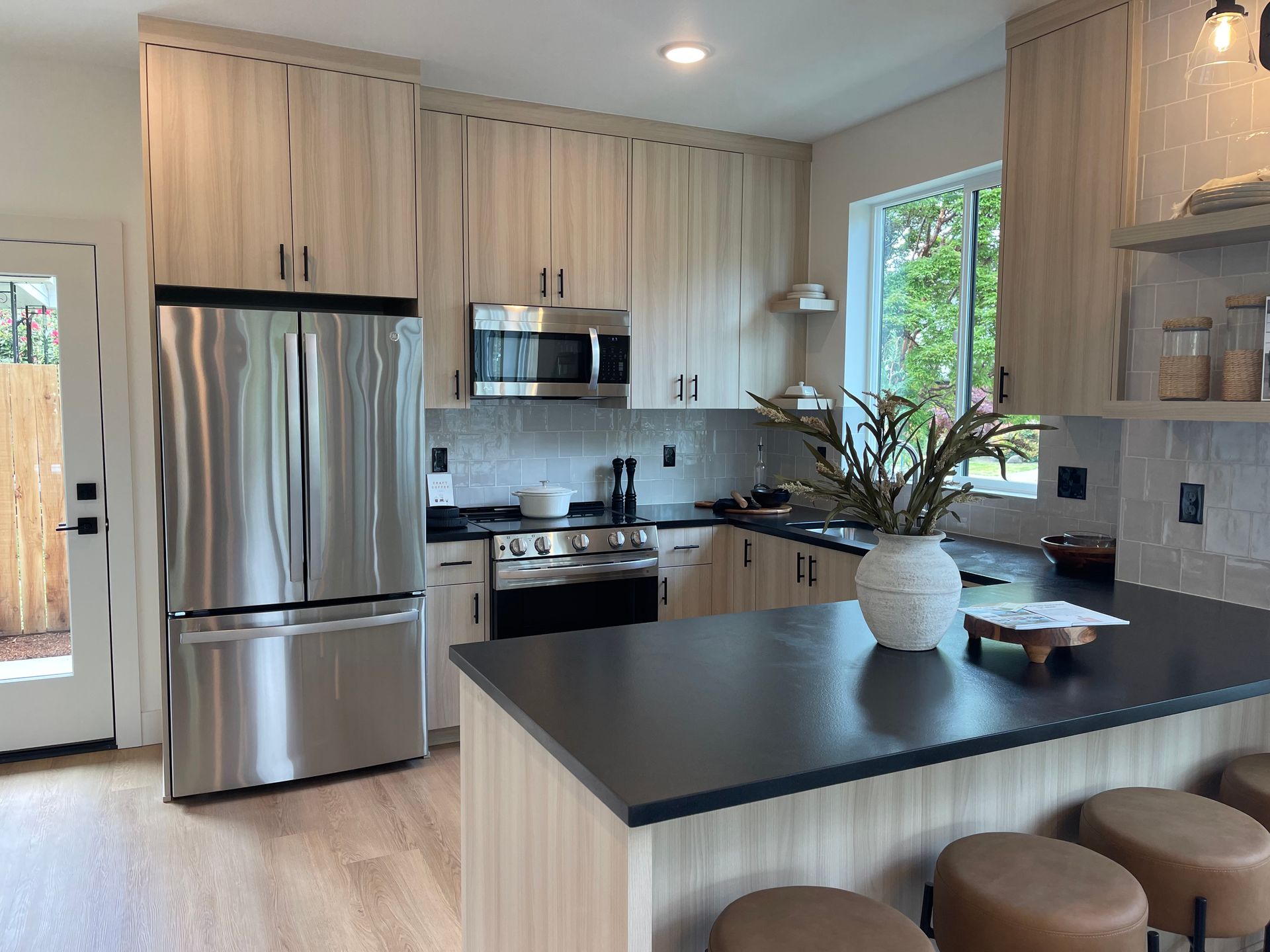 Modern kitchen with light wood cabinets, stainless steel appliances, and a black countertop island.