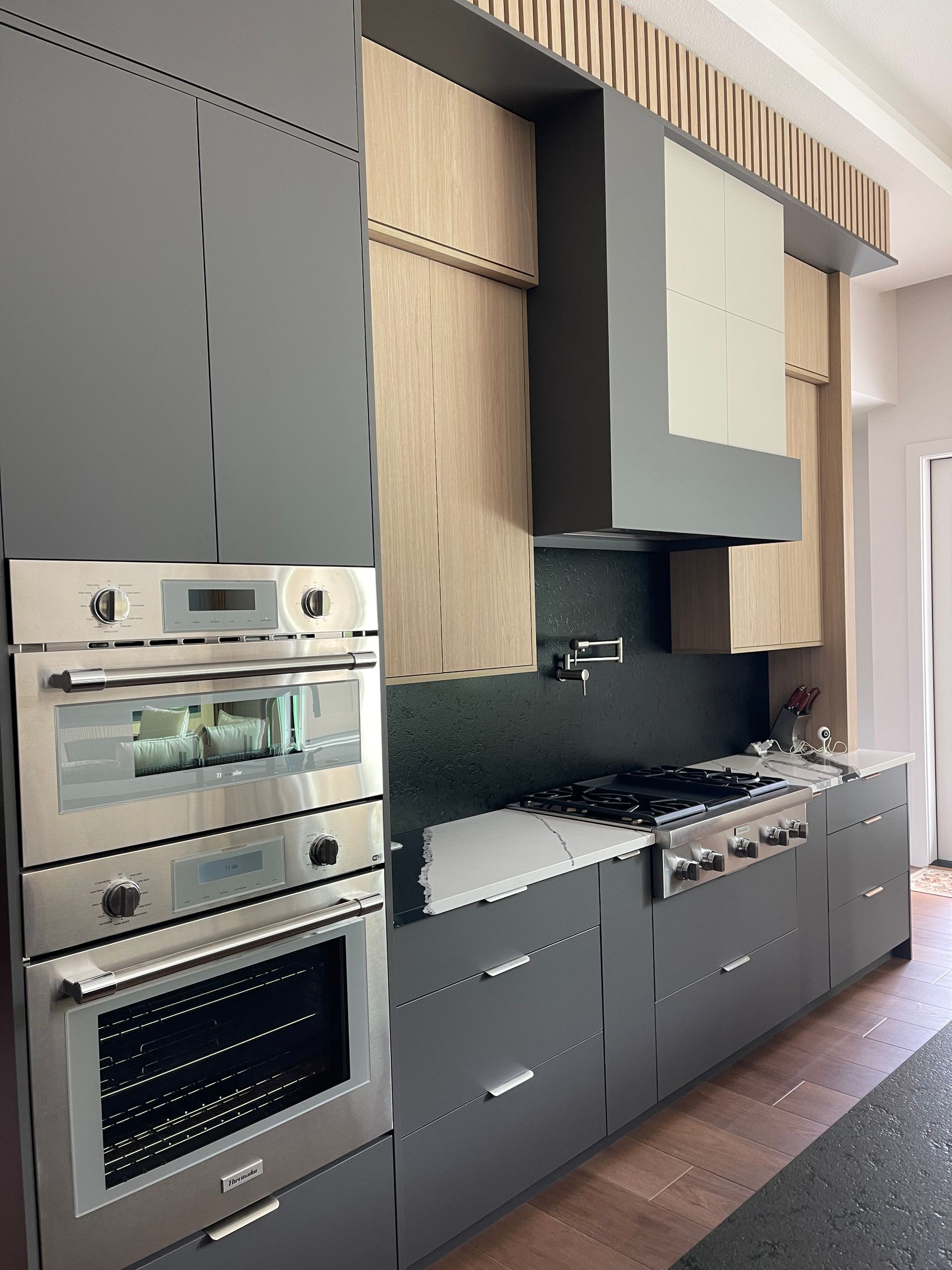 Modern kitchen with gray cabinets, stainless steel appliances, and wood accents.
