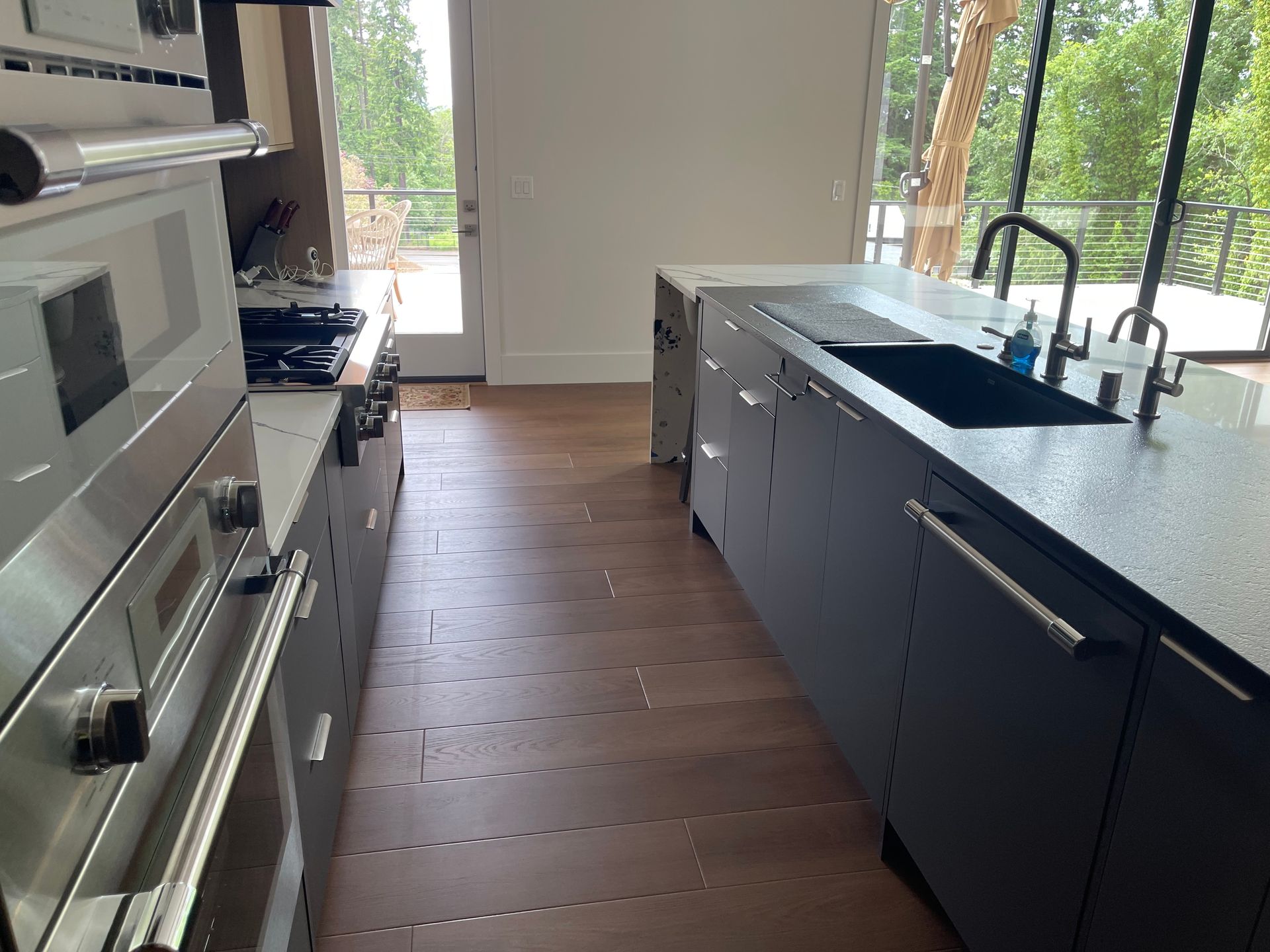 Modern kitchen with dark cabinetry, stainless steel appliances, and island with a sink, facing a window.