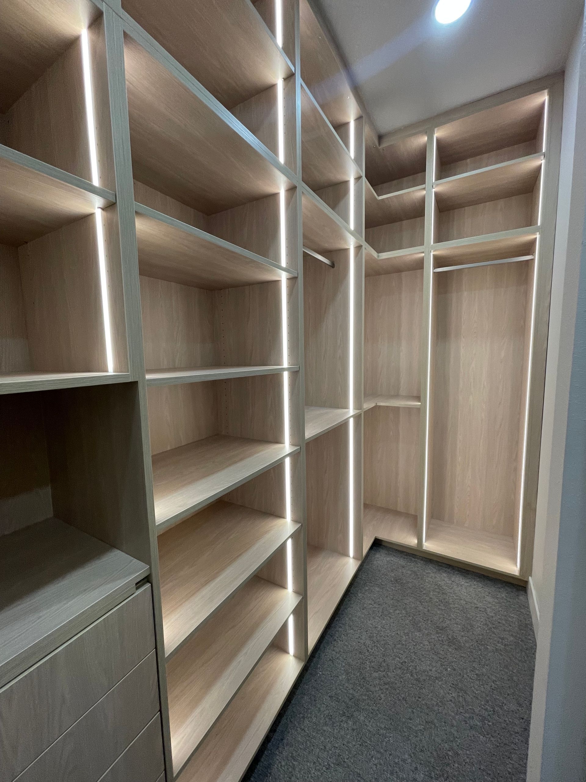 Empty walk-in closet with light wood shelves, white panels, and gray carpet.