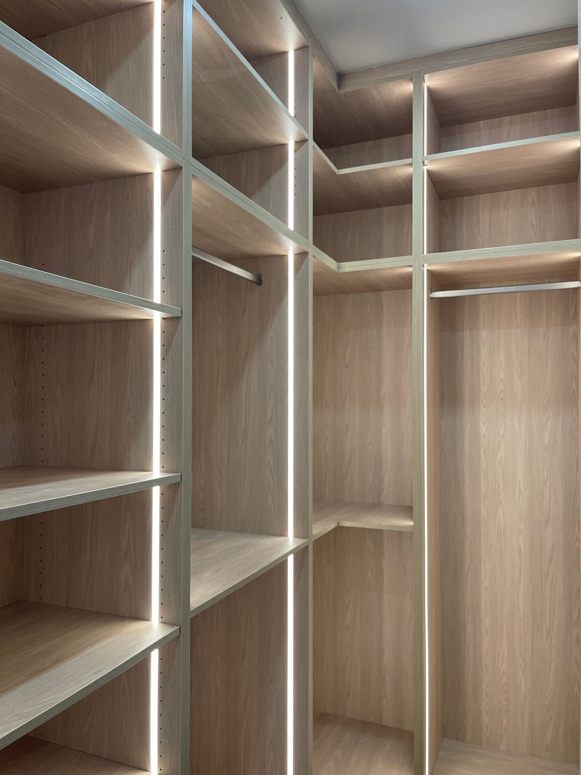 Empty built-in wooden closet with shelves and hanging rods, viewed from the inside