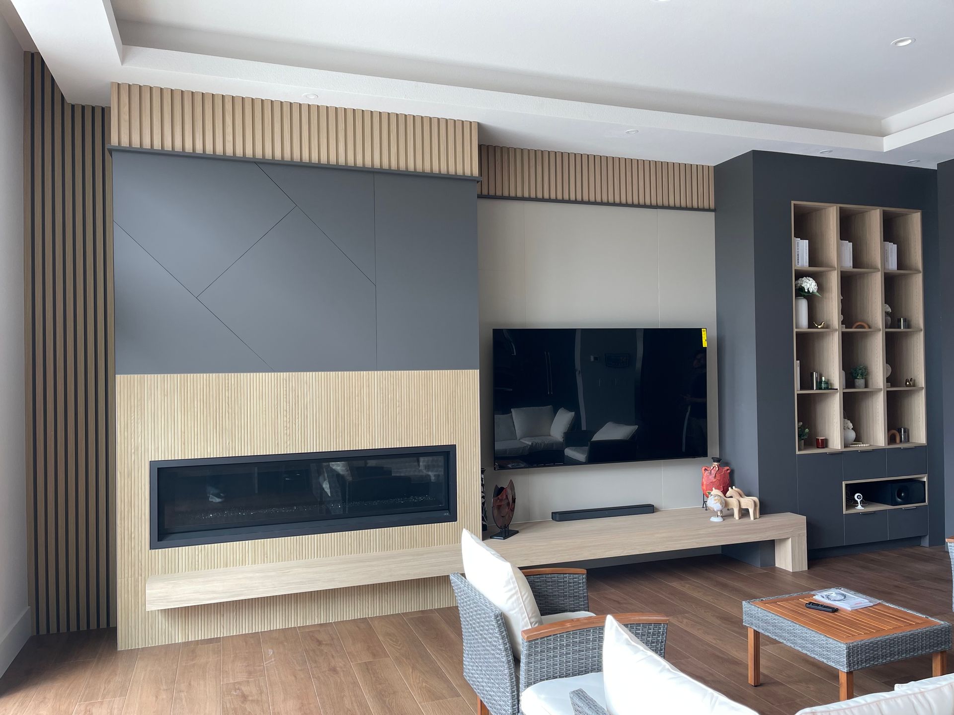 Modern living room with fireplace, built-in shelves, TV. Light wood paneling, gray and beige accents, wooden floor.